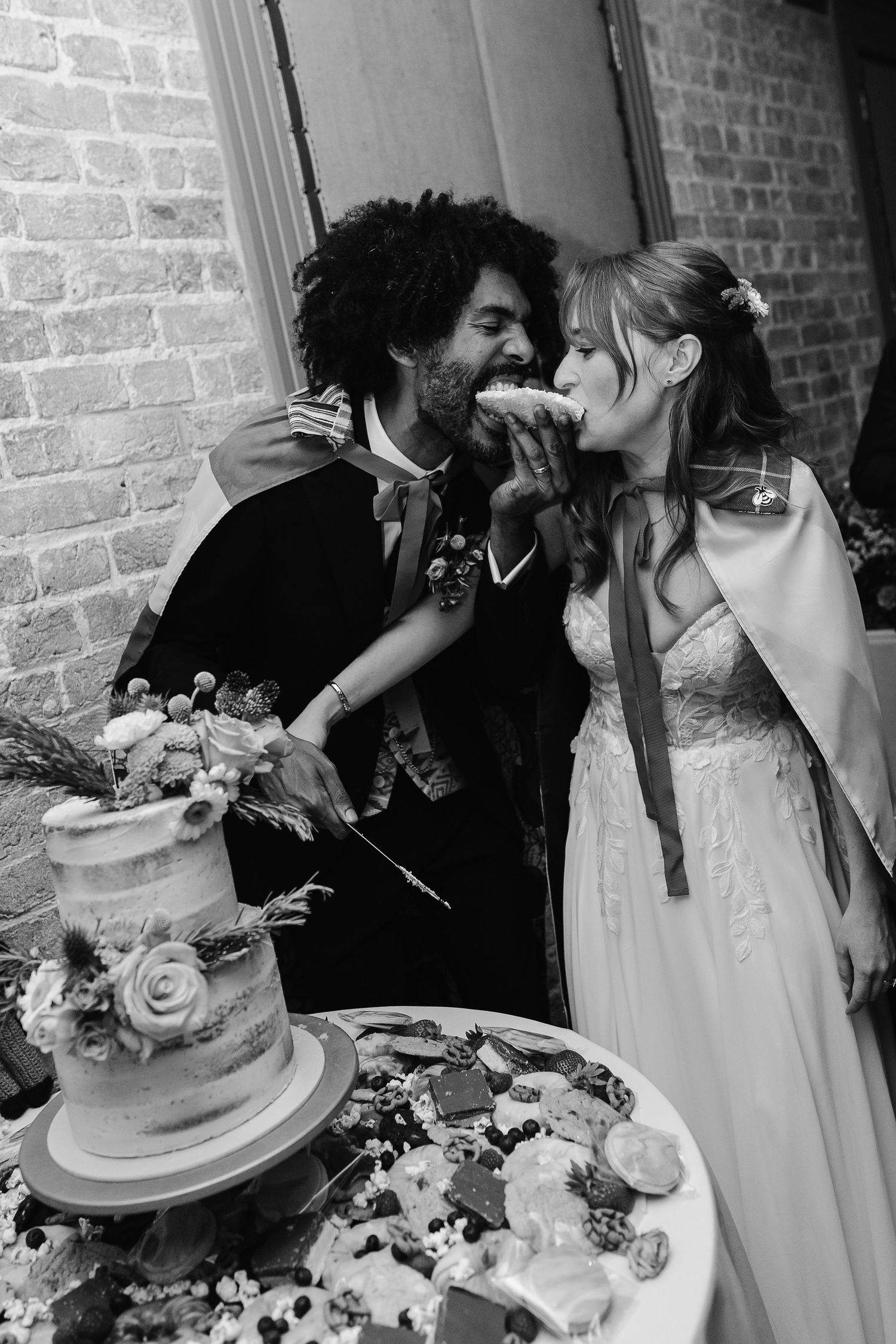 Black and white photo of bride and groom sharing cake bite at wedding reception.