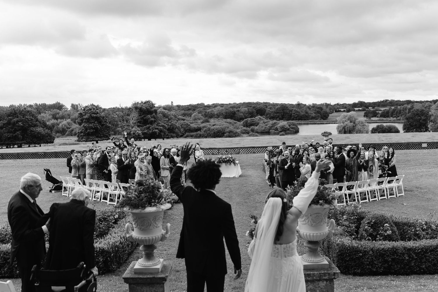 Black and white photo of bride and groom walking toward cheering guests at grand estate wedding.