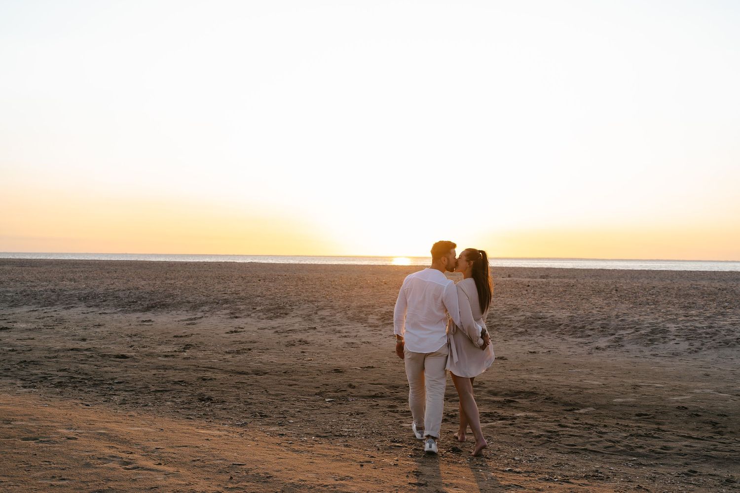 Couple walking hand in hand on a sandy beach, silhouetted against a breathtaking golden sunset.