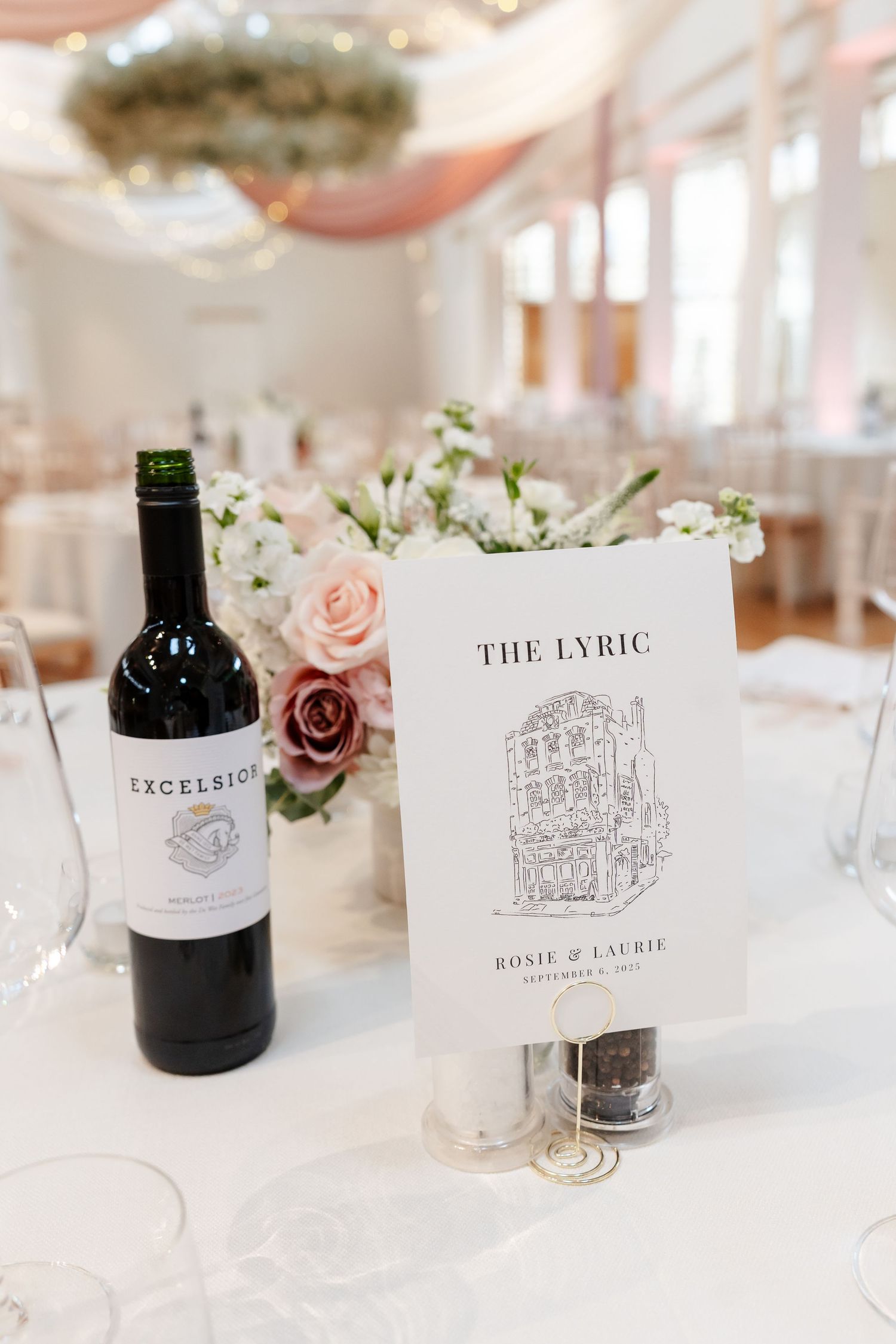 Elegant wedding table setting with Excelsior red wine, floral centerpiece, and The Lyric table name card.