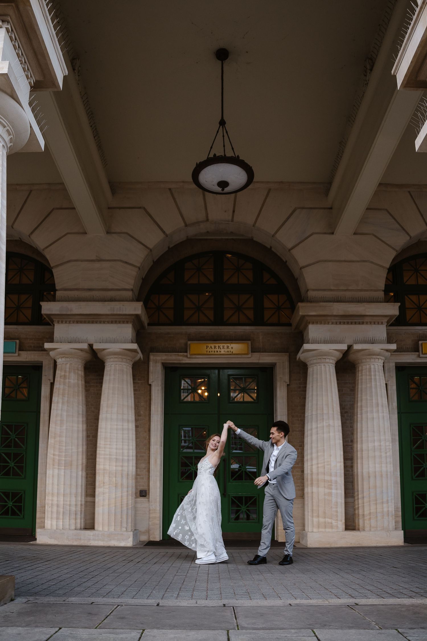 Bride and groom dance together outside ornate building with green arched doors.
