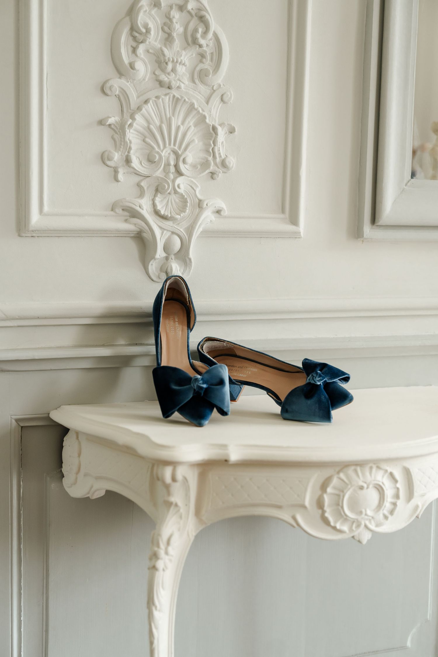 Elegant navy blue velvet bow heels displayed on white ornate French console table for wedding day.