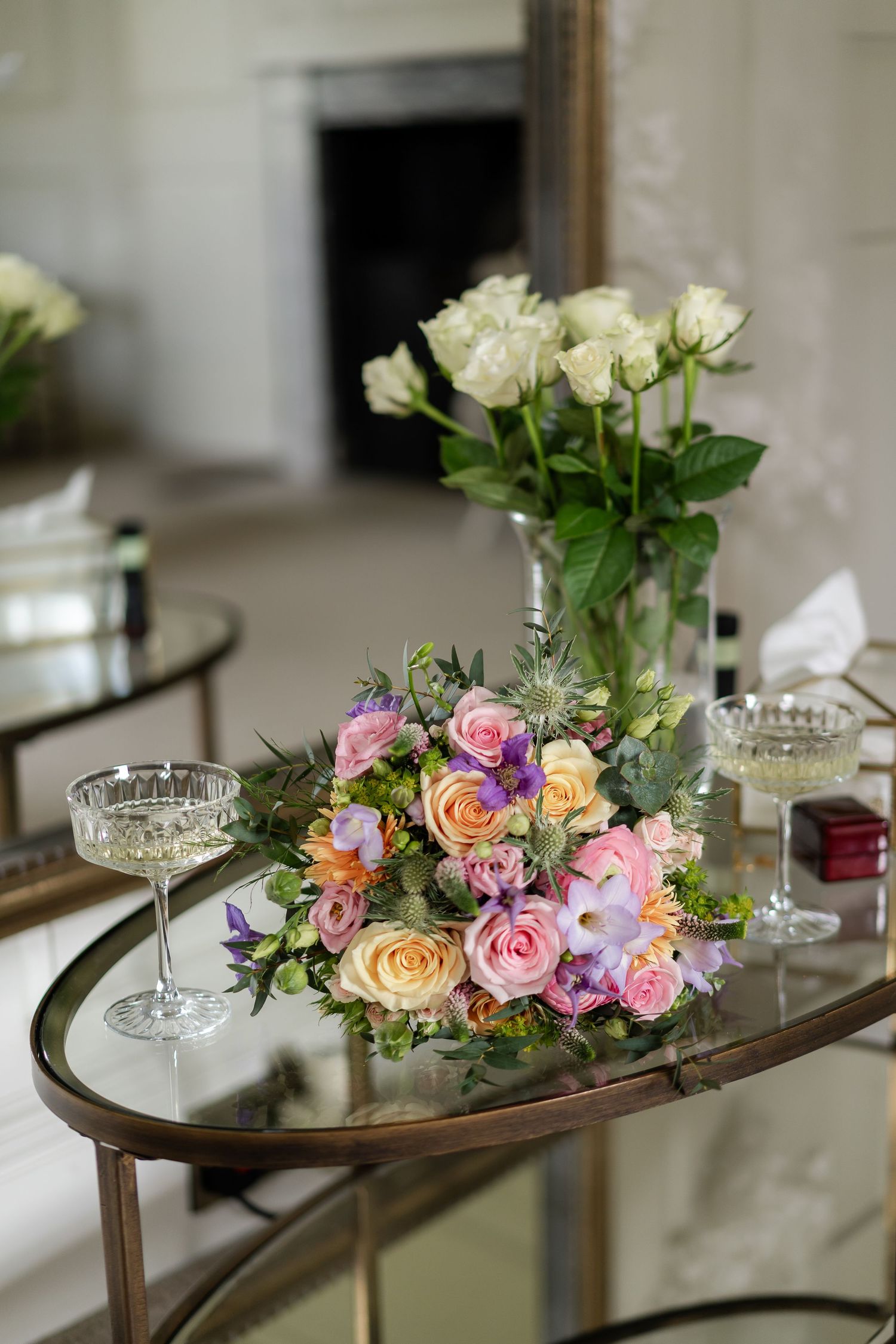 Elegant wedding bouquet with pink and purple flowers on mirrored table with champagne glasses and white roses at Lincolnshires Wootton Hall