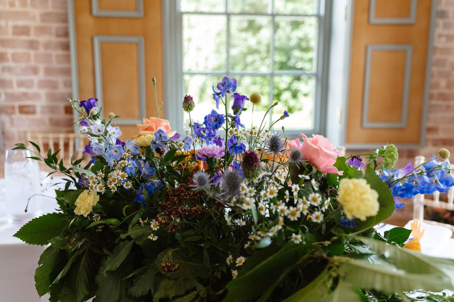 Wildflower wedding centerpiece with blue, pink, and white blooms on a white tablecloth.