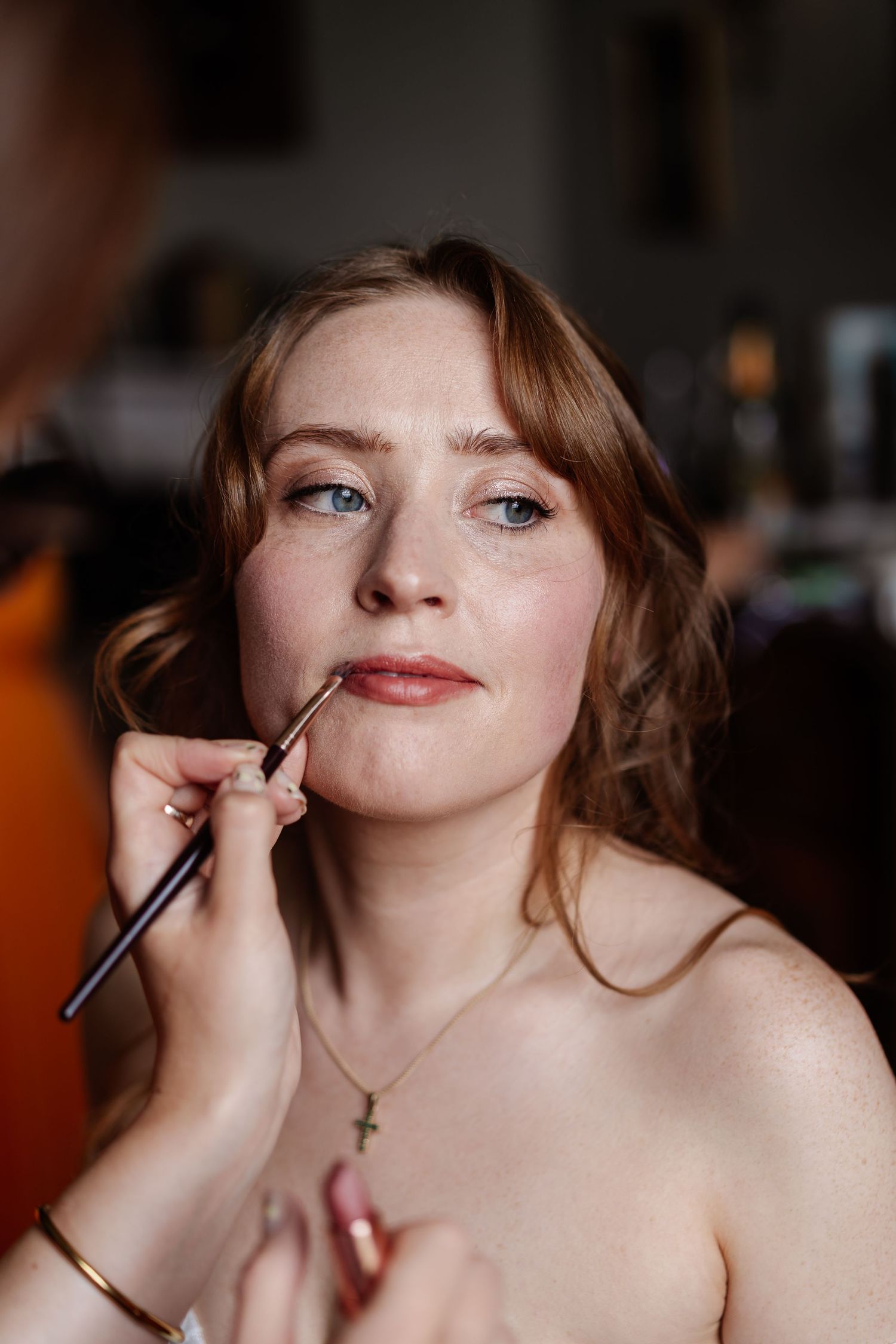 Professional makeup artist applying lip liner to red-haired bride during wedding preparation.