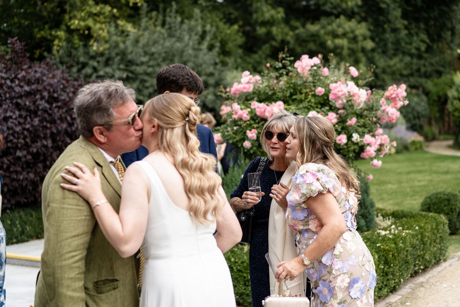 Guests mingling outdoors at a wedding reception with pink roses blooming in the background.