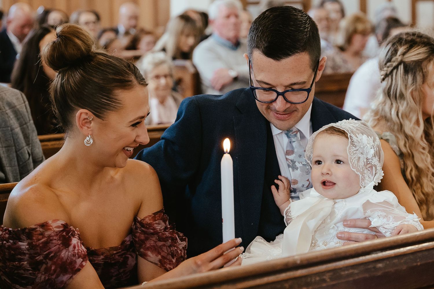 Family with baby holding a candle during a christening ceremony in a church.