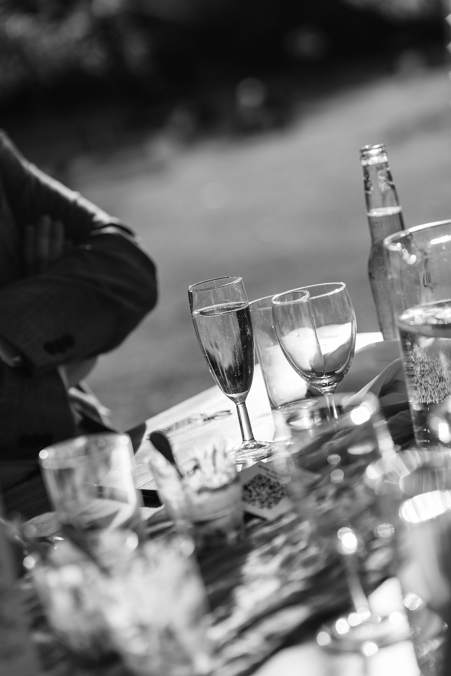 Black and white photo of empty champagne flutes and glasses on outdoor wedding reception table.