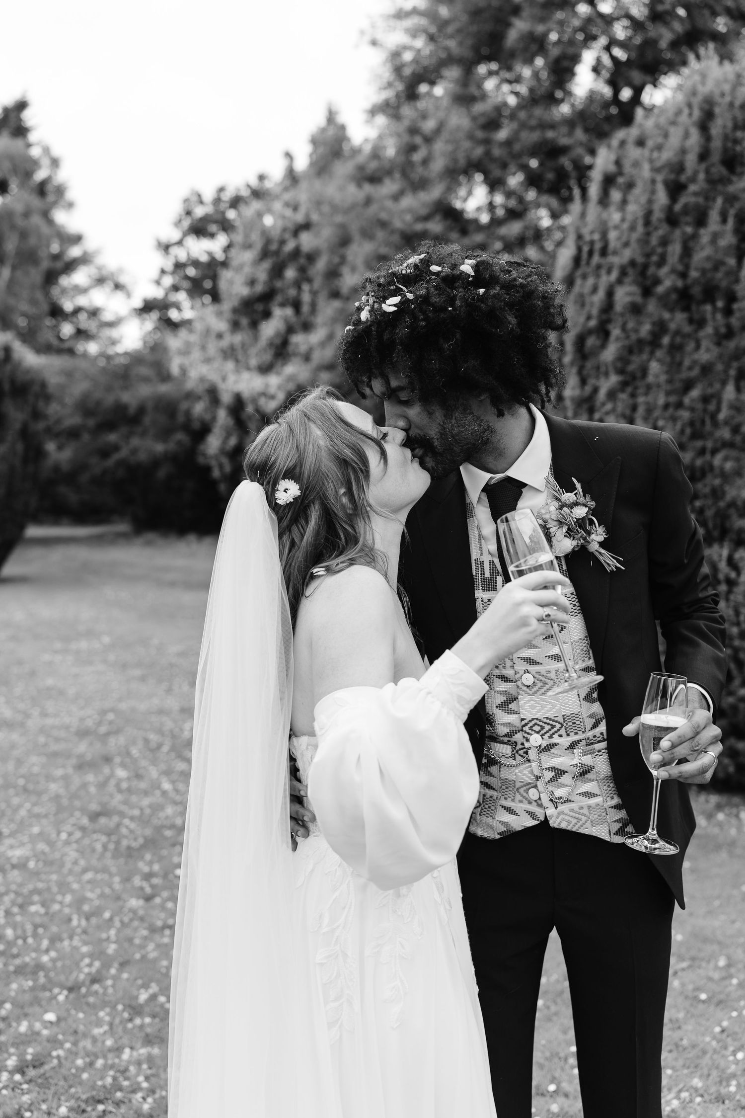 Black and white romantic photo of bride and groom sharing a kiss while holding champagne glasses.