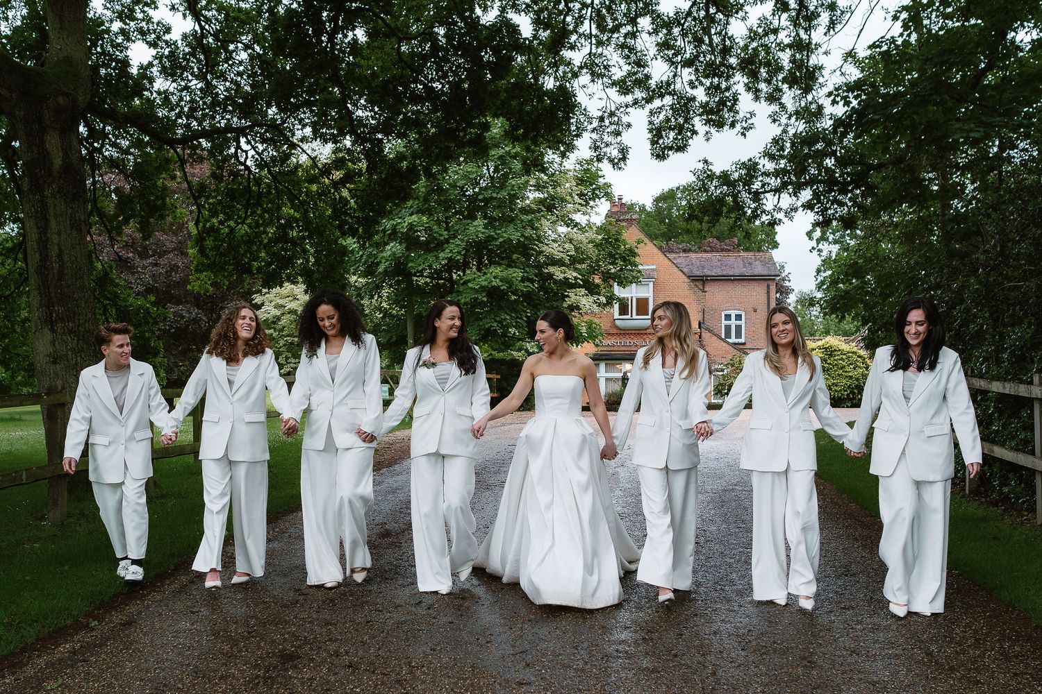 Hannah and her bridesmaids holding hand in their crisp white bridesmaids suits and luxury Vera Wang gown. Luxury Wedding