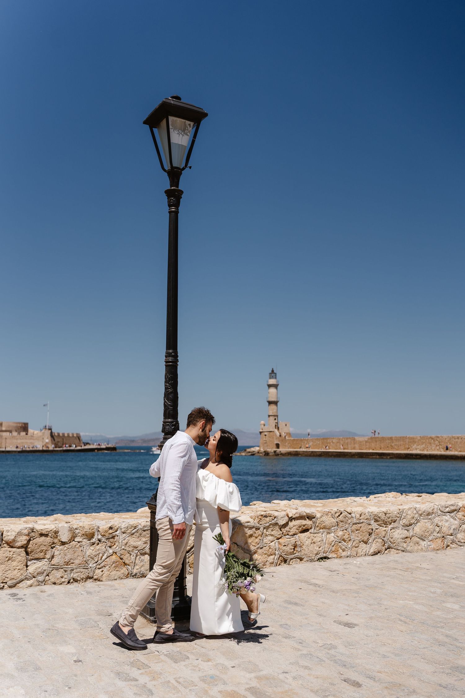 Wedding couple sharing a kiss under a street lamp at the scenic Chania harbor in Crete, Greece.