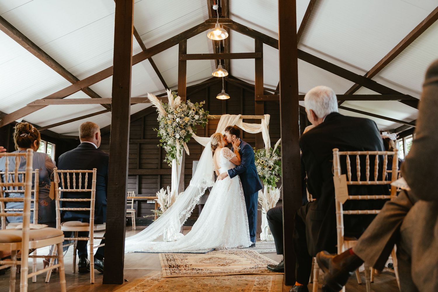 bride and groom kissing at the alter in a rustic norfolk barn with exposed beams.