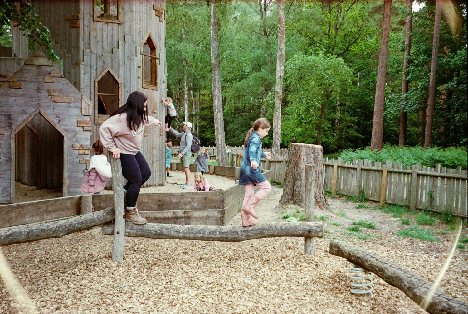 Children playing on wooden stumps in a nature-inspired castle playground surrounded by trees.
