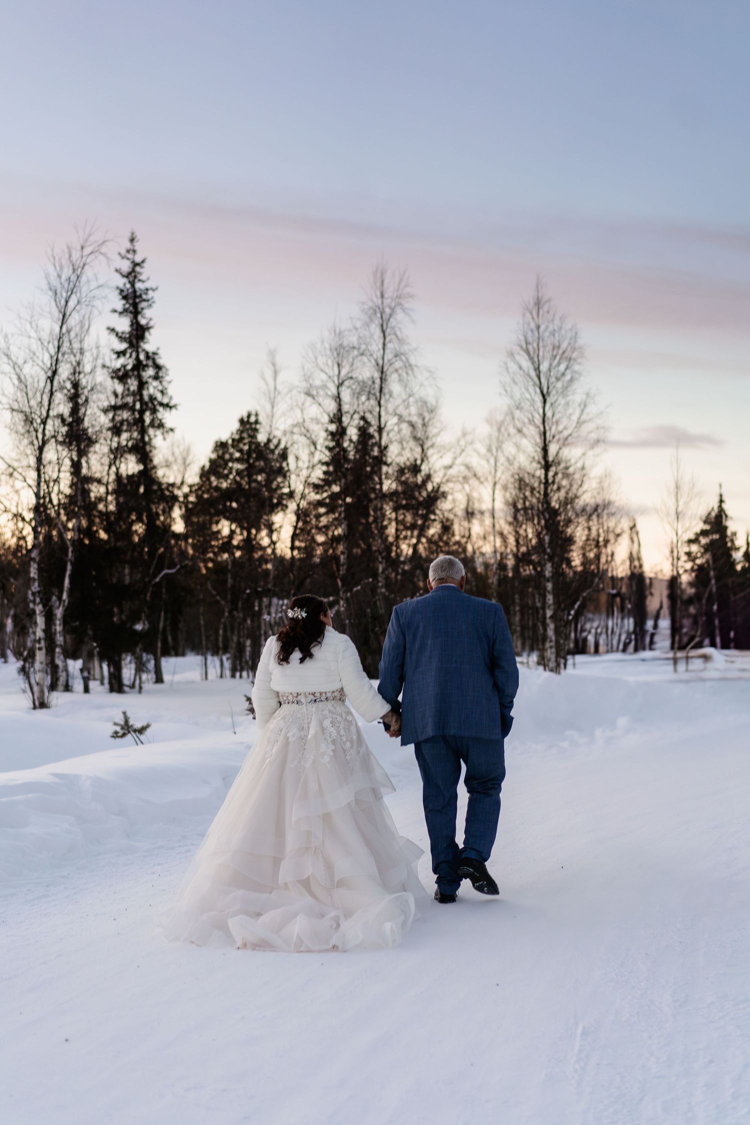 Couple candidly walking through forest with pink skies. Luxury Lapland wedding photographer. Snow wedding. Mountain Wedding.