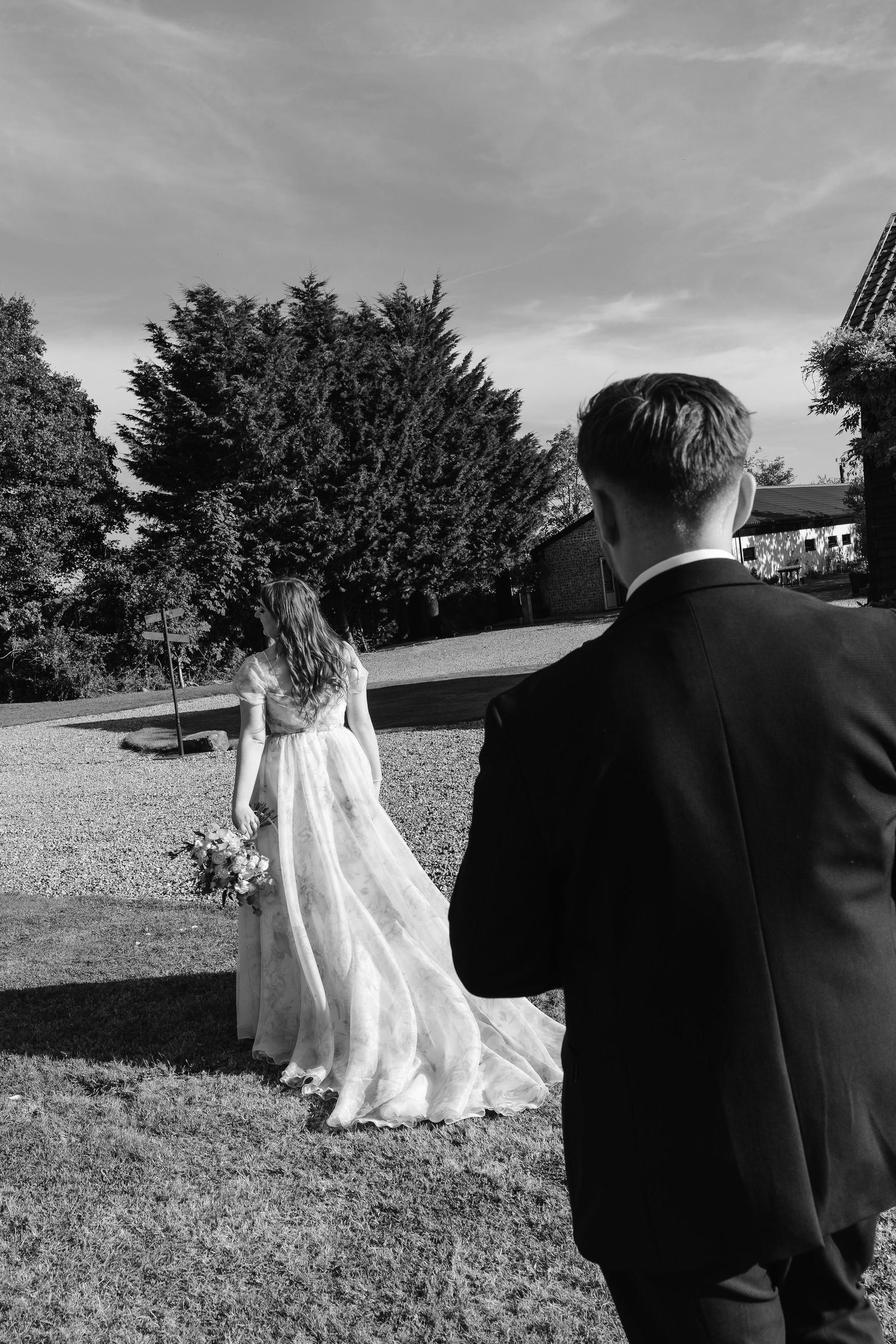 Black and white photo of bride and groom walking across manicured grounds on their wedding day.