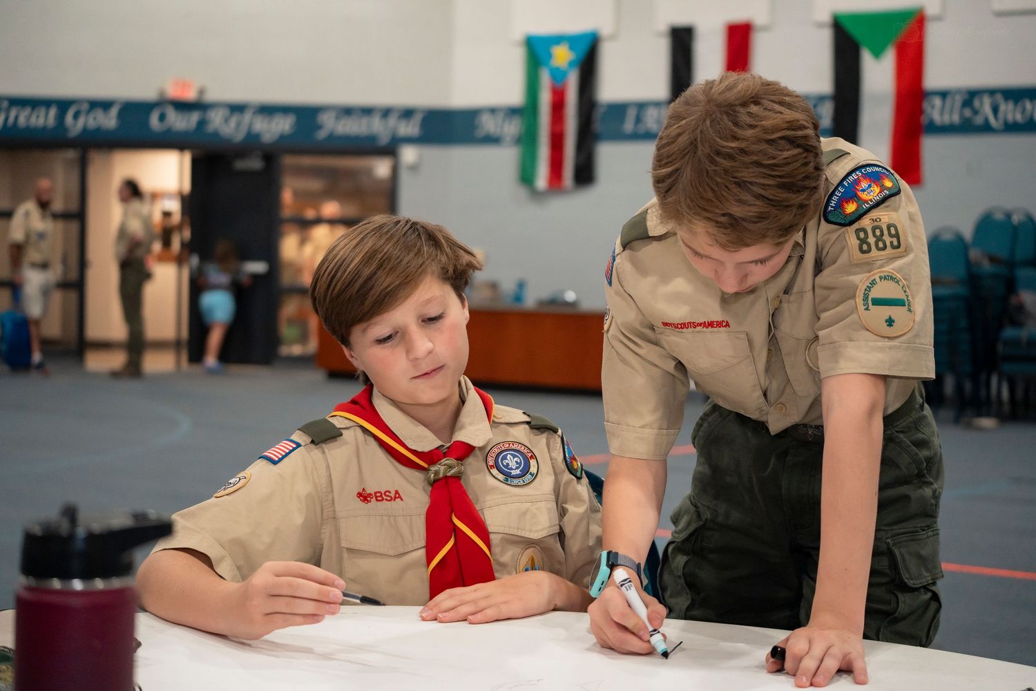 Two Boy Scouts work together on a document at a table during a scouting event.