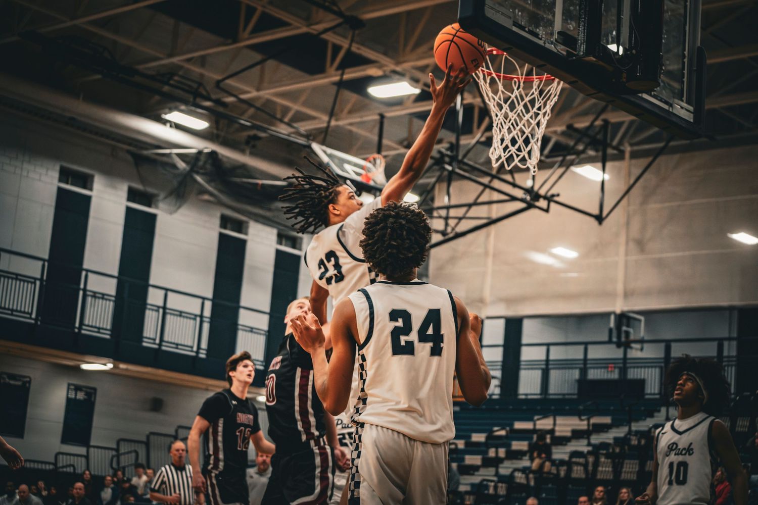 Basketball player dunks over defender number 24 during an intense high school indoor basketball game.