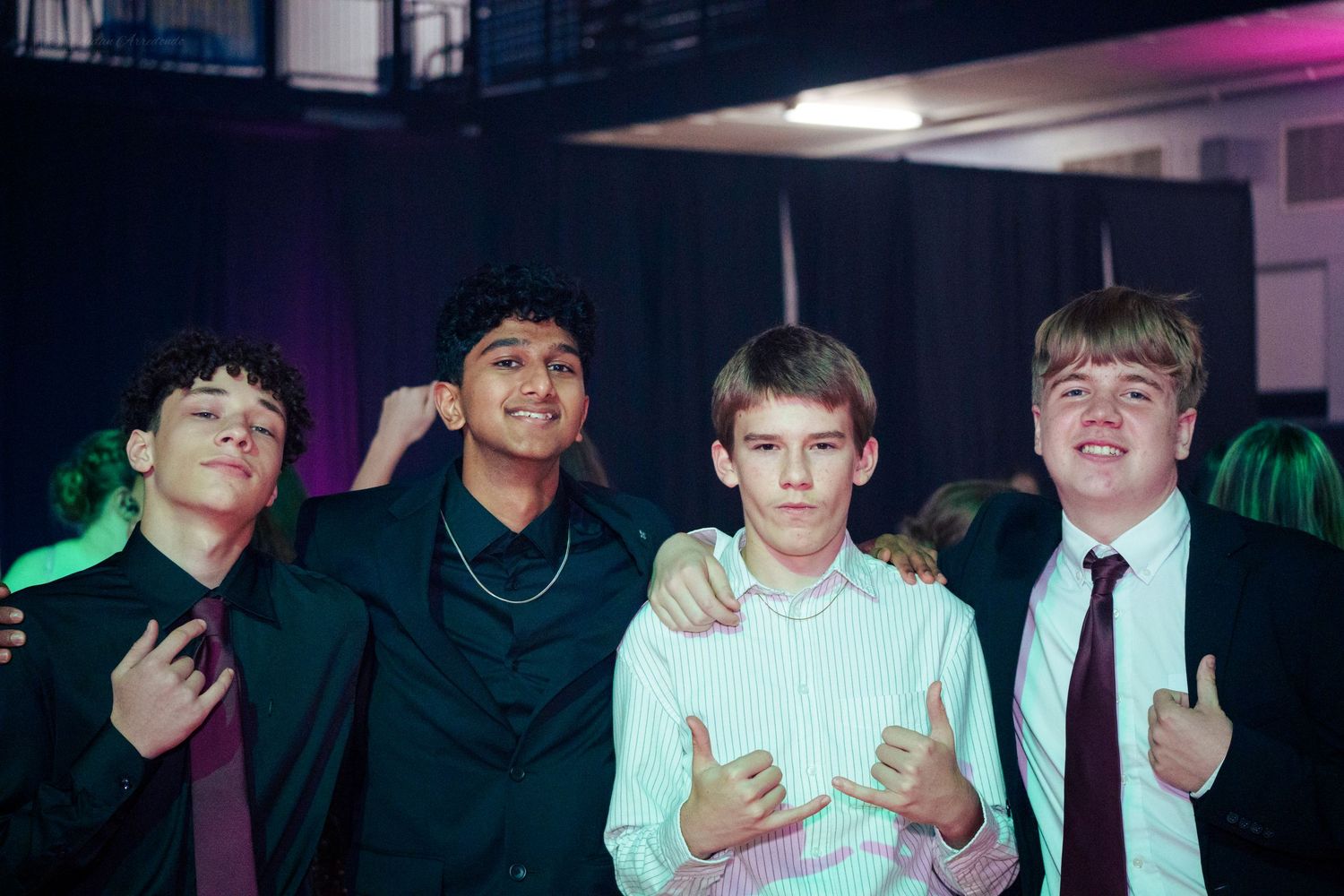 Four teenage boys posing together at a school formal event, dressed in suits and smart casual attire.