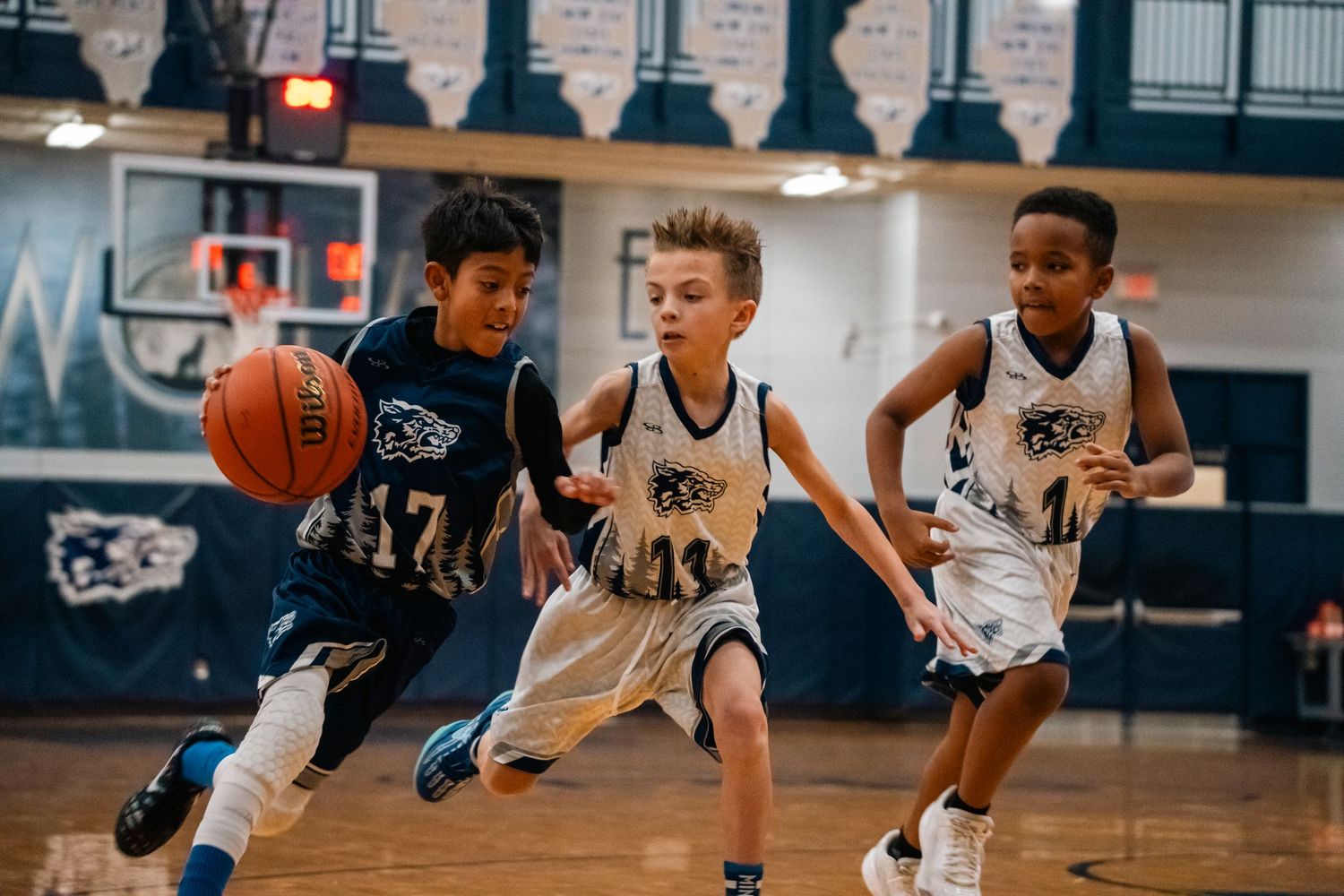 Young boys playing competitive youth basketball game in a school gymnasium, dribbling and defending.