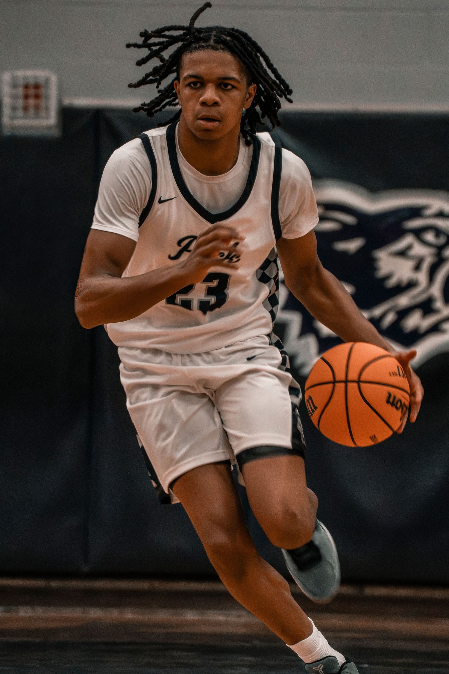 Young basketball player number 23 dribbling down the court in a white uniform during a game.