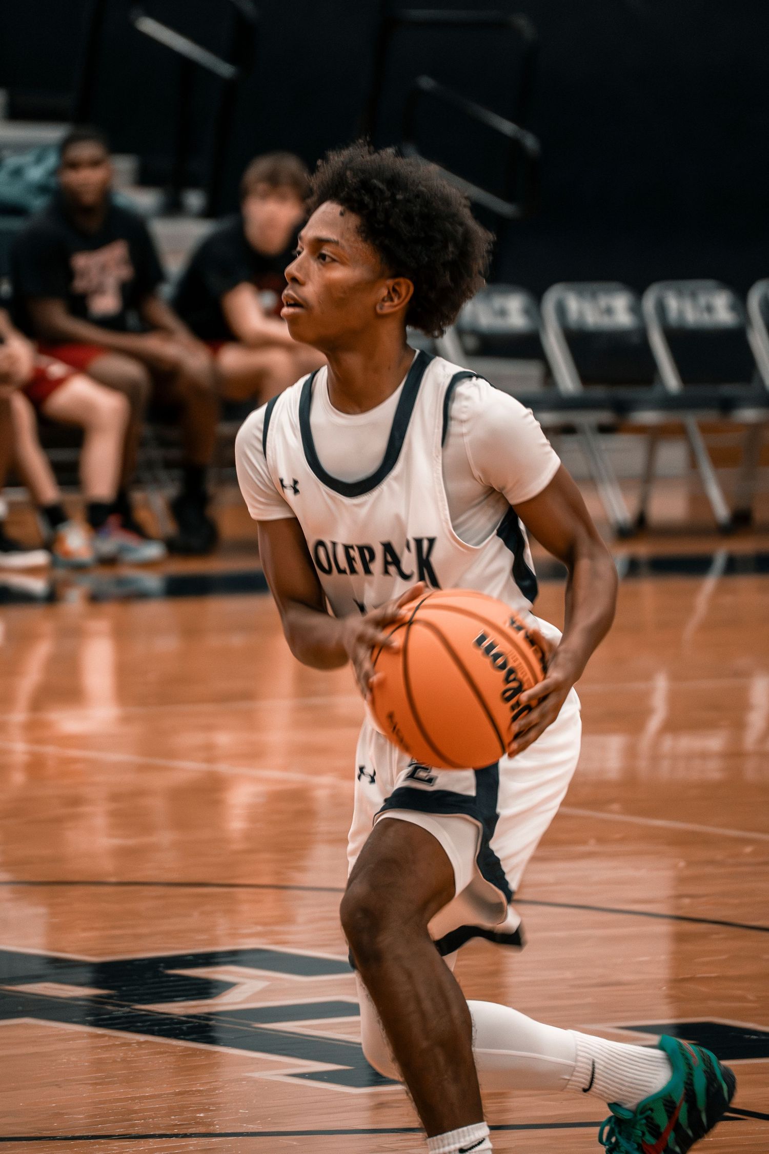Wolfpack basketball player dribbles ball on court during a competitive high school indoor basketball game.