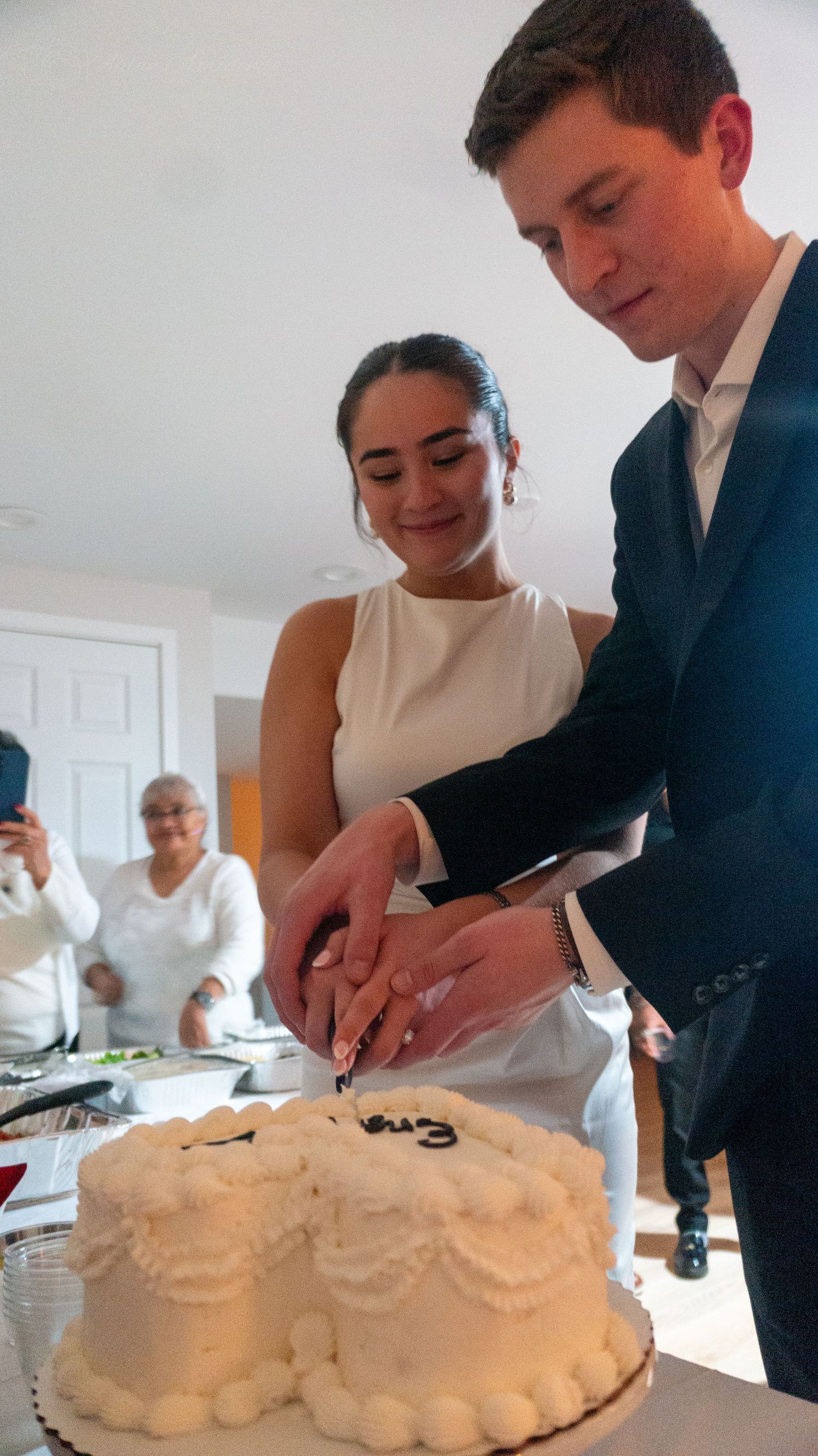 Newlywed couple cutting their white wedding cake together at an intimate indoor wedding reception.