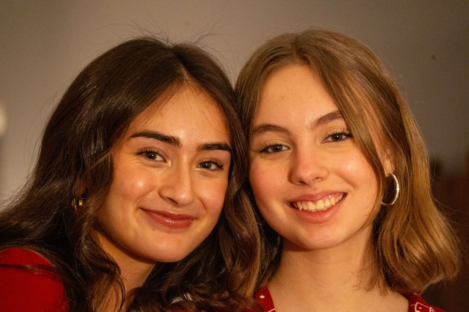 Two smiling teenage girls pose closely together for a photo at an indoor event.