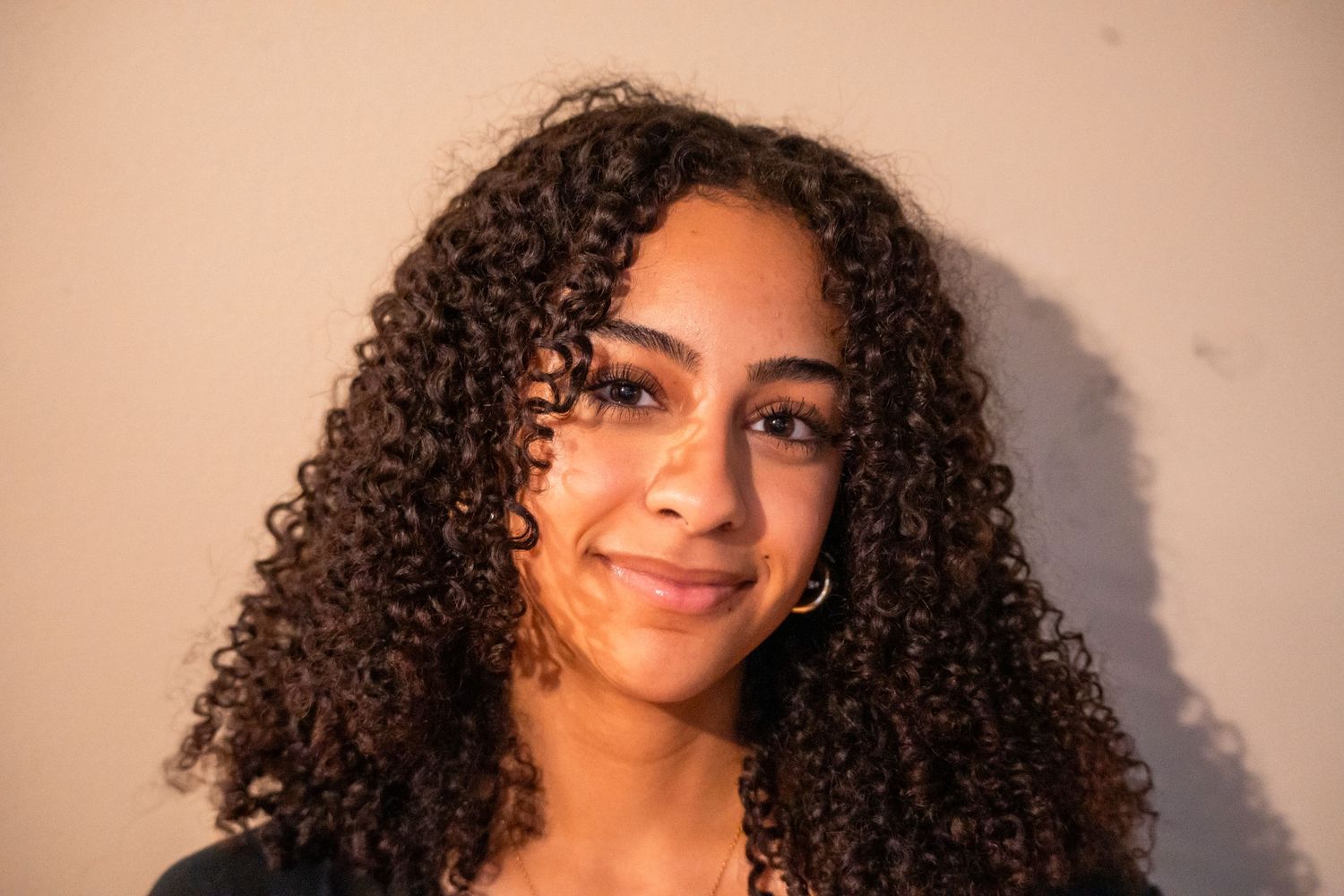 Young woman with curly hair smiling softly against a neutral background.