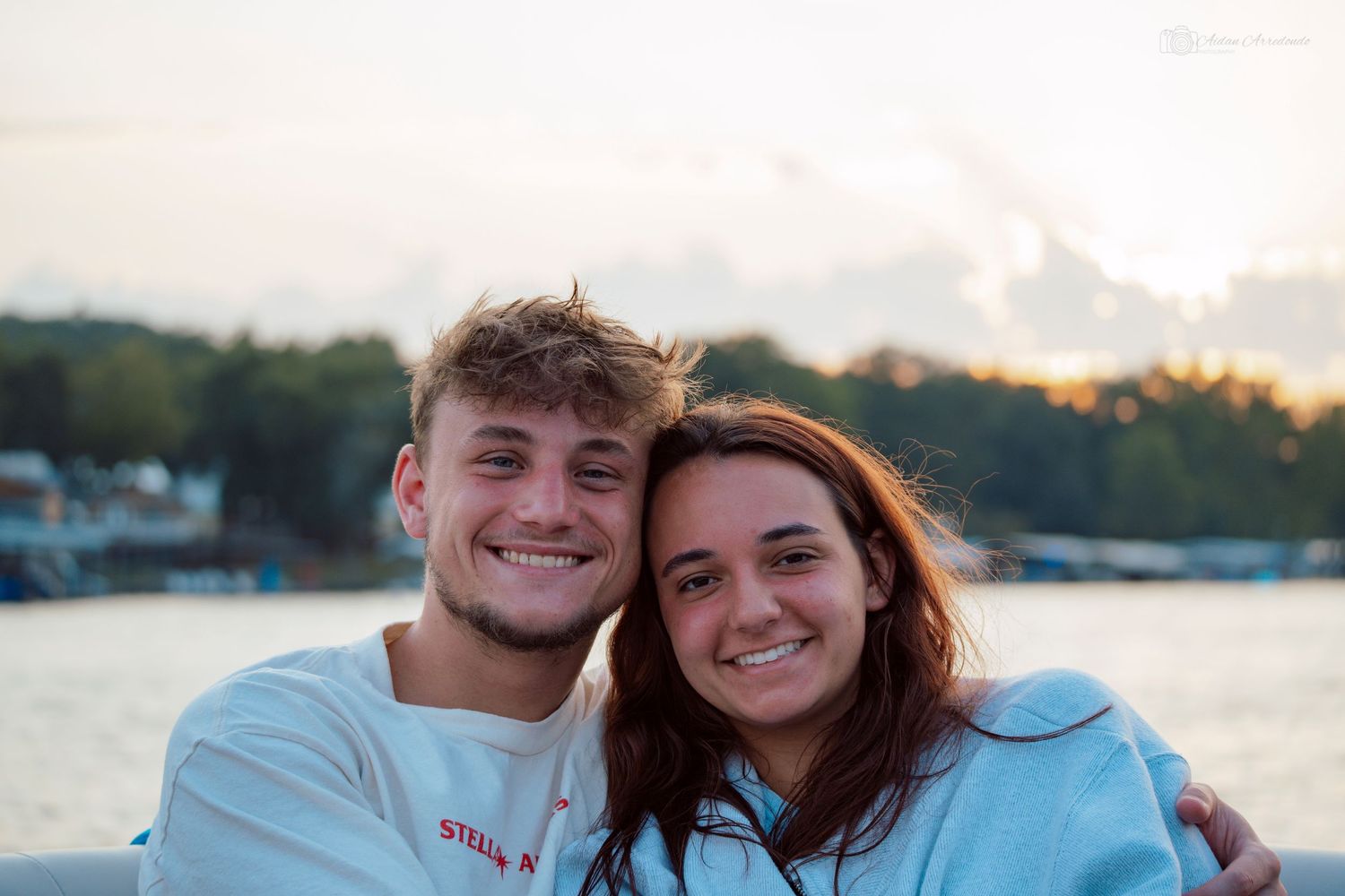 Smiling young couple posing together near a lake at sunset.