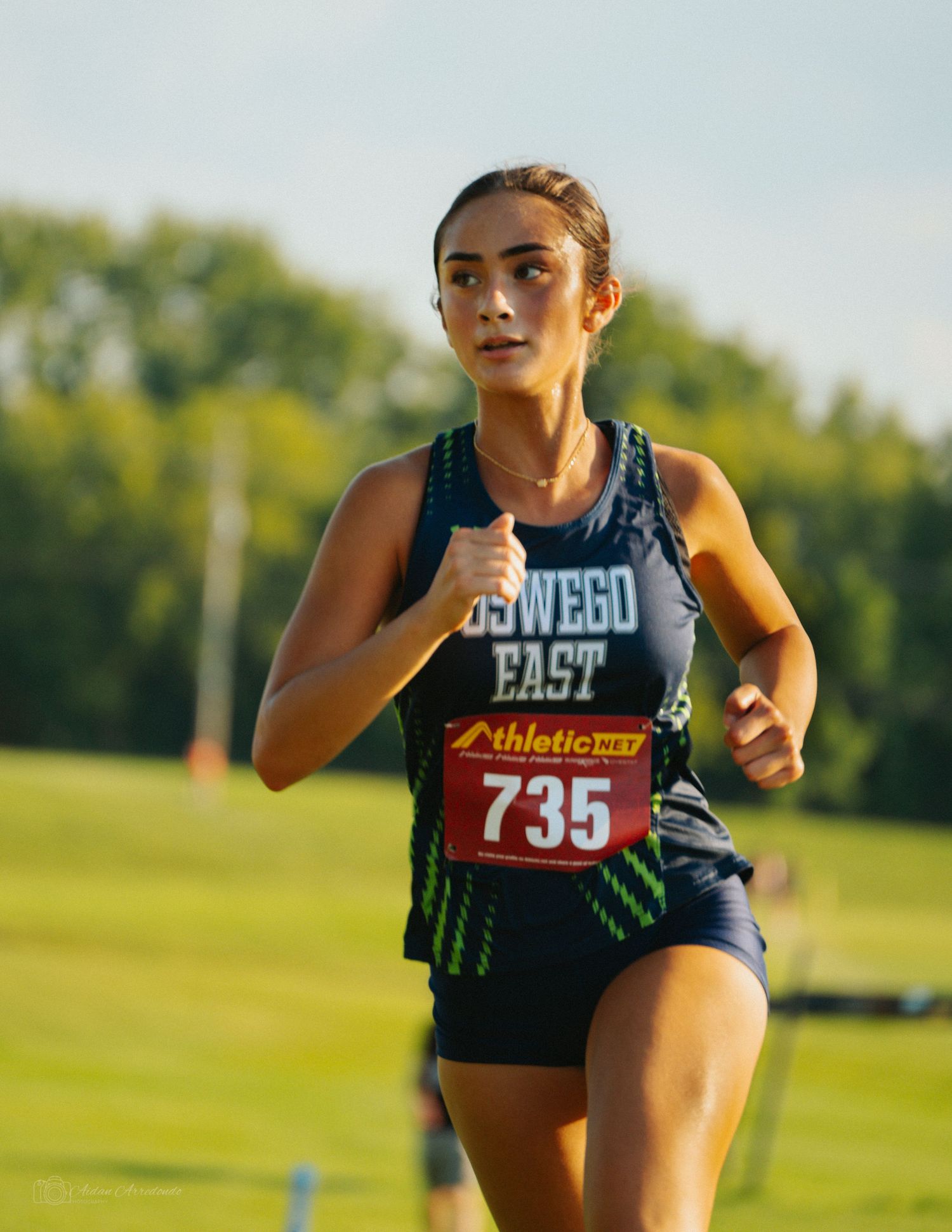 Female cross country runner in Oswego East jersey number 735 competes in an outdoor athletic meet.