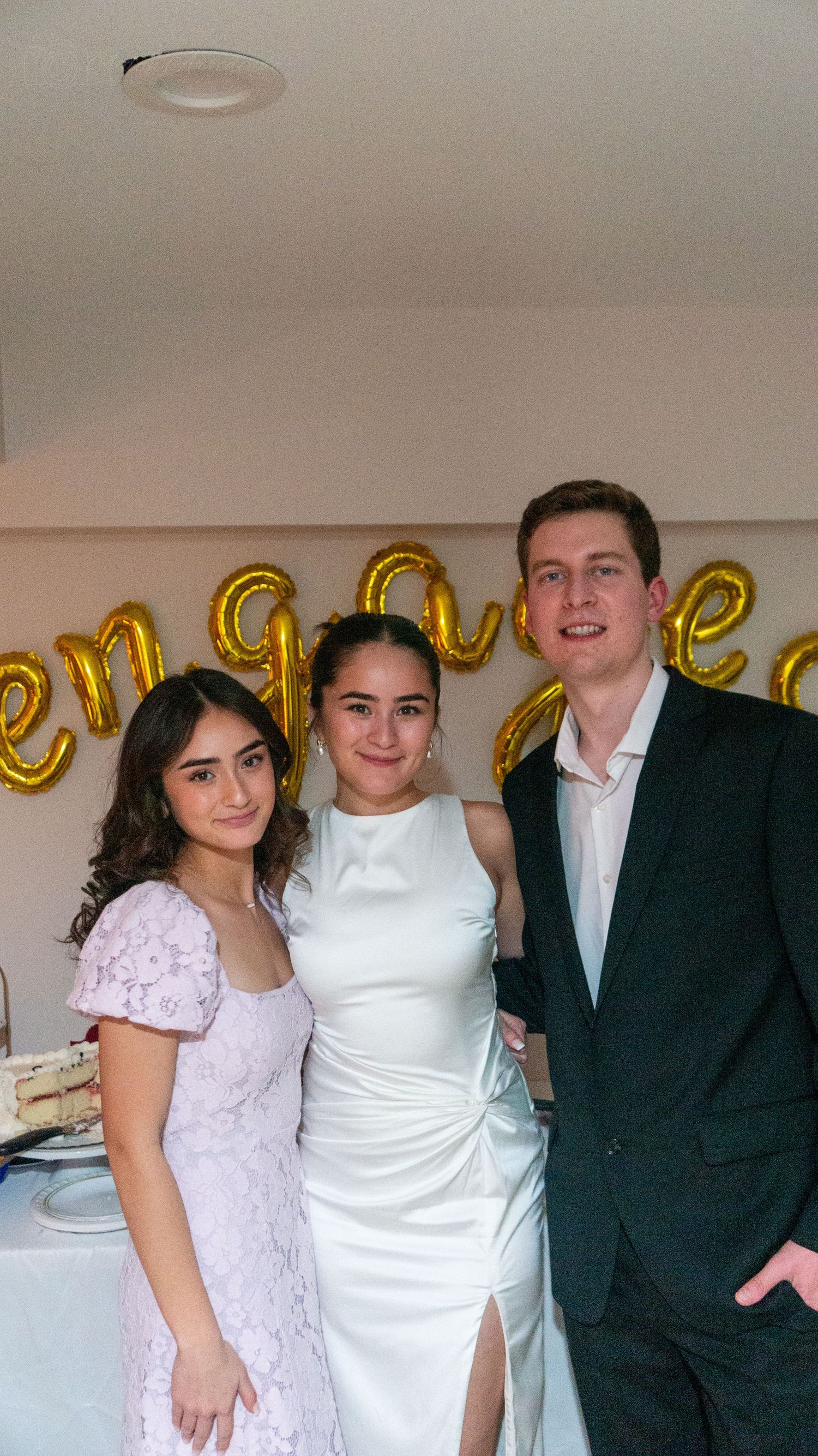 Couple and friend posing in front of gold engaged balloon letters at an engagement party celebration.