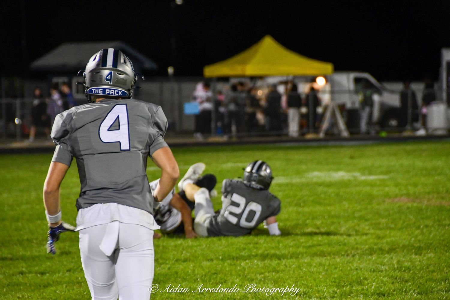 Football player wearing number 4 gray Pack jersey walks on night game sideline with teammate nearby.