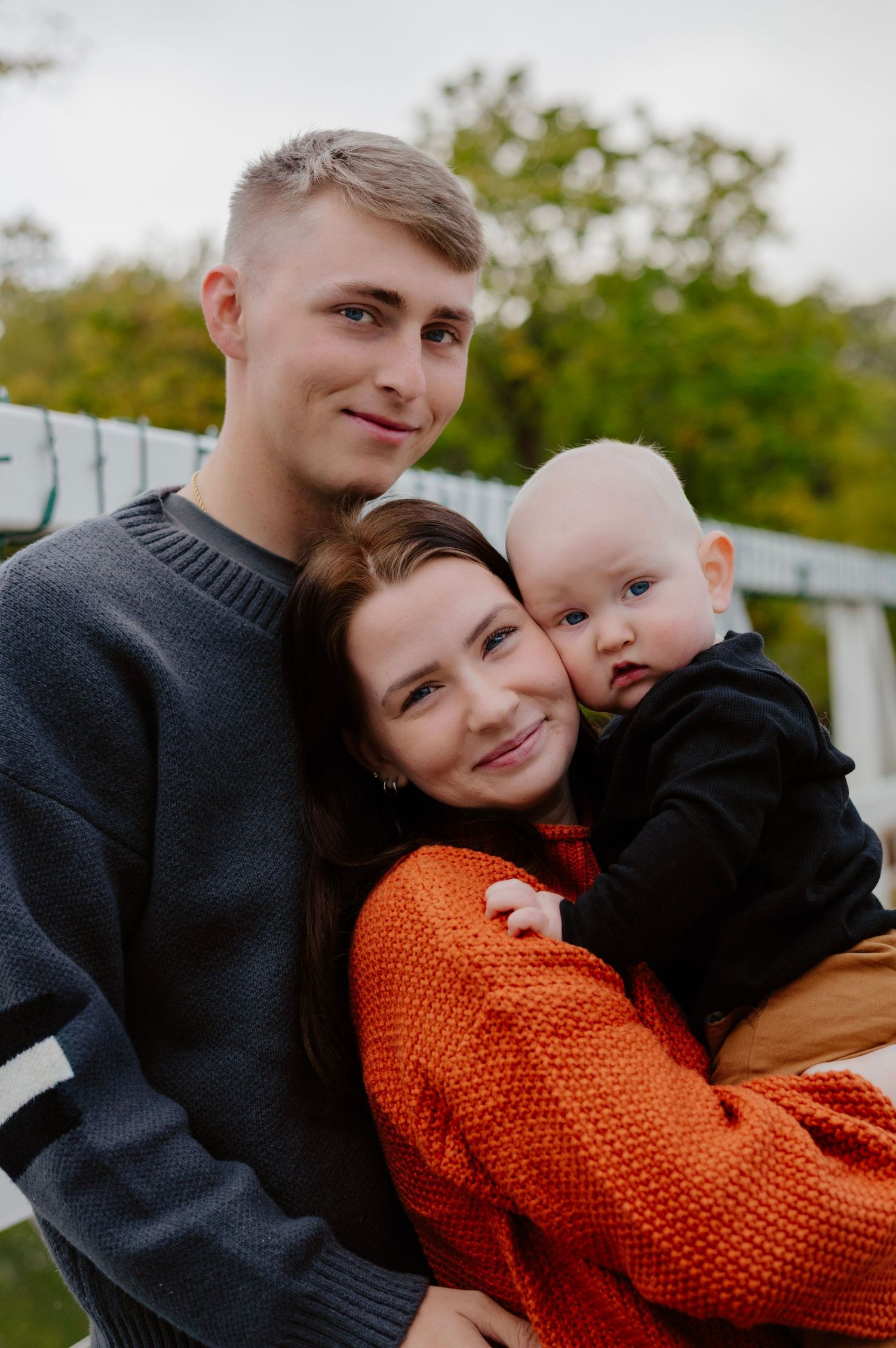 Intimate family portrait outdoors with orange sweater and grey knit against fall backdrop.