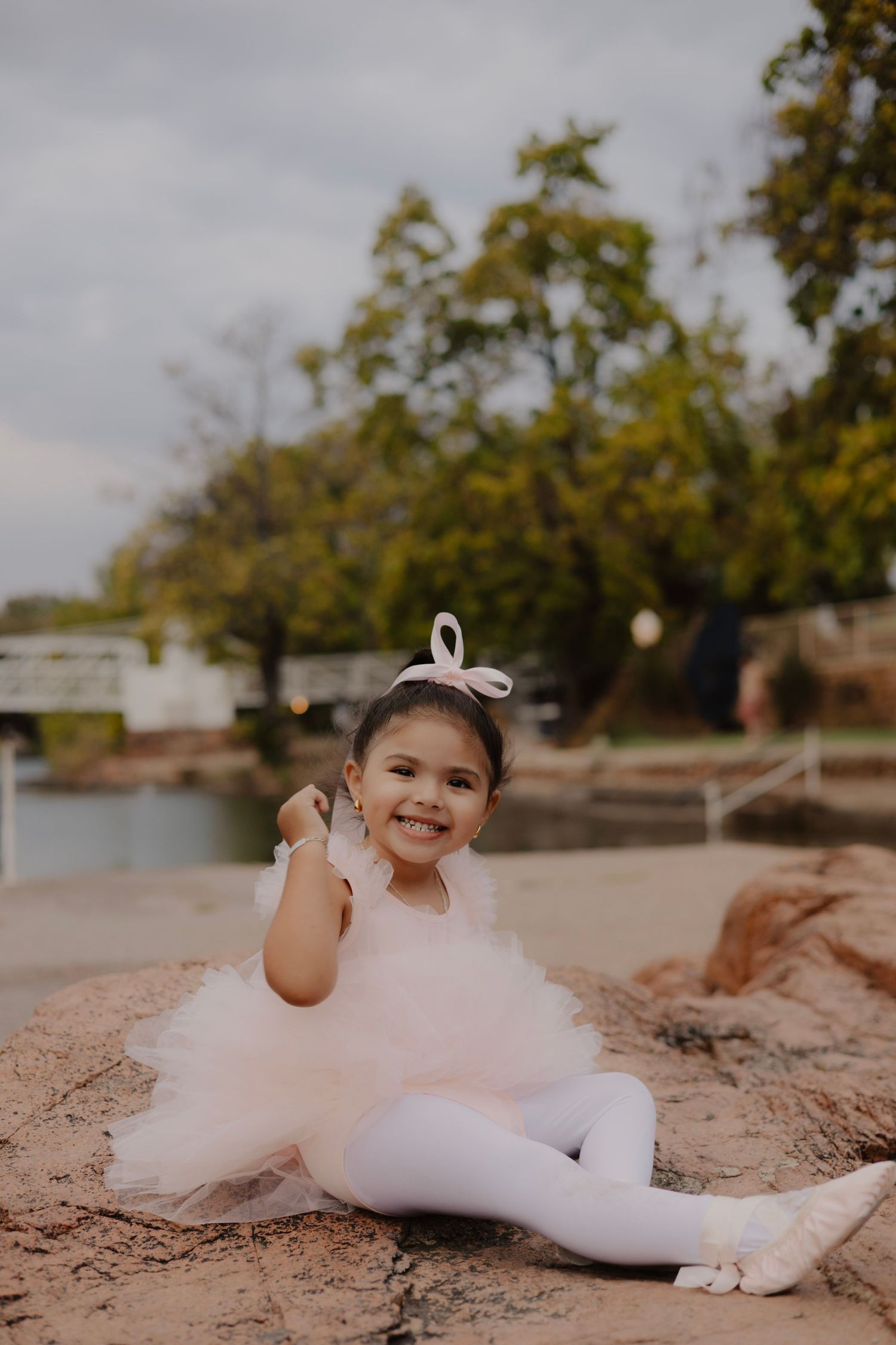 Young dancer in white tutu poses gracefully on sandy ground during outdoor photoshoot.