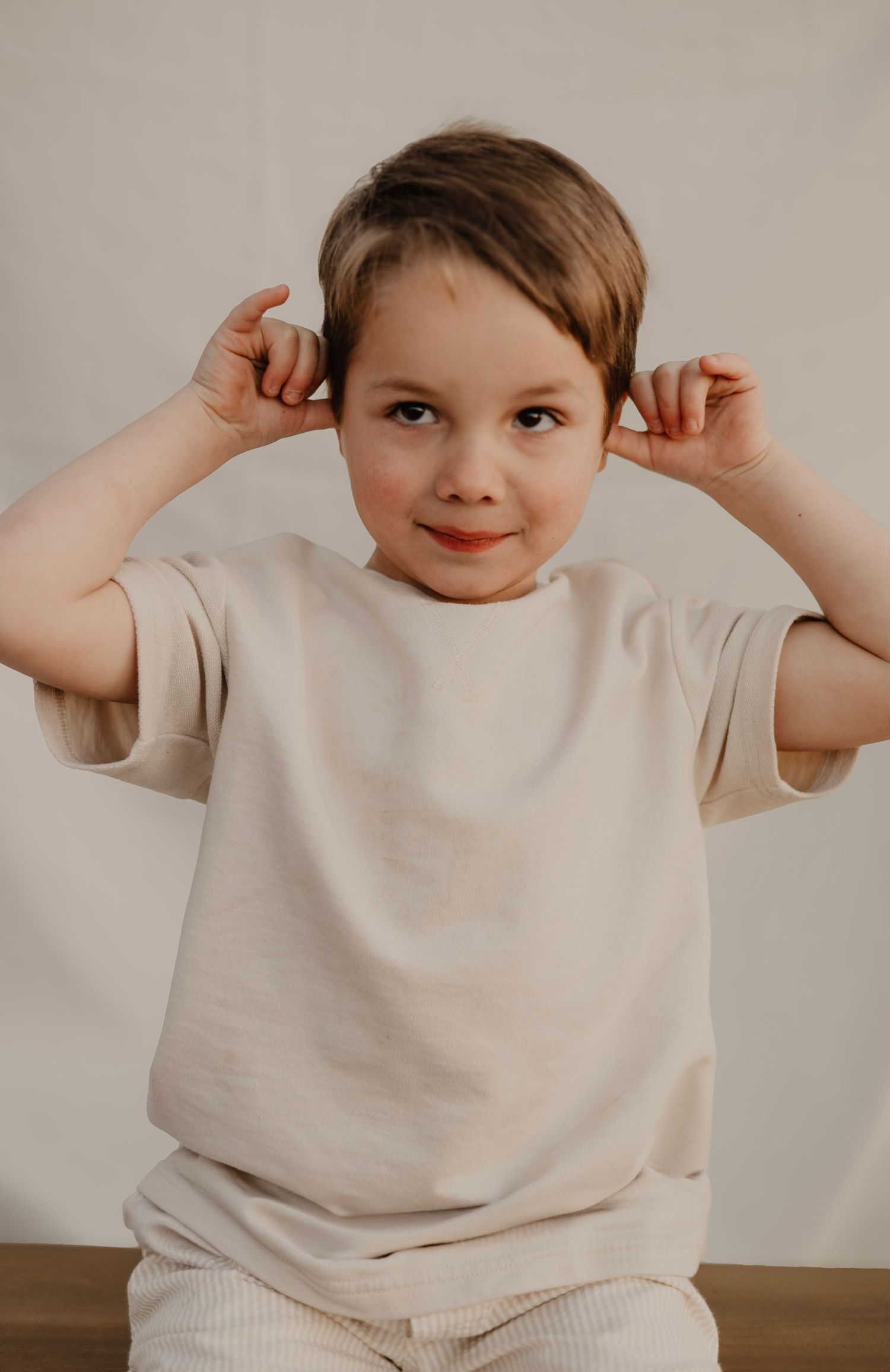 Young child in beige shirt making playful expressions in sequence of photos against neutral background.