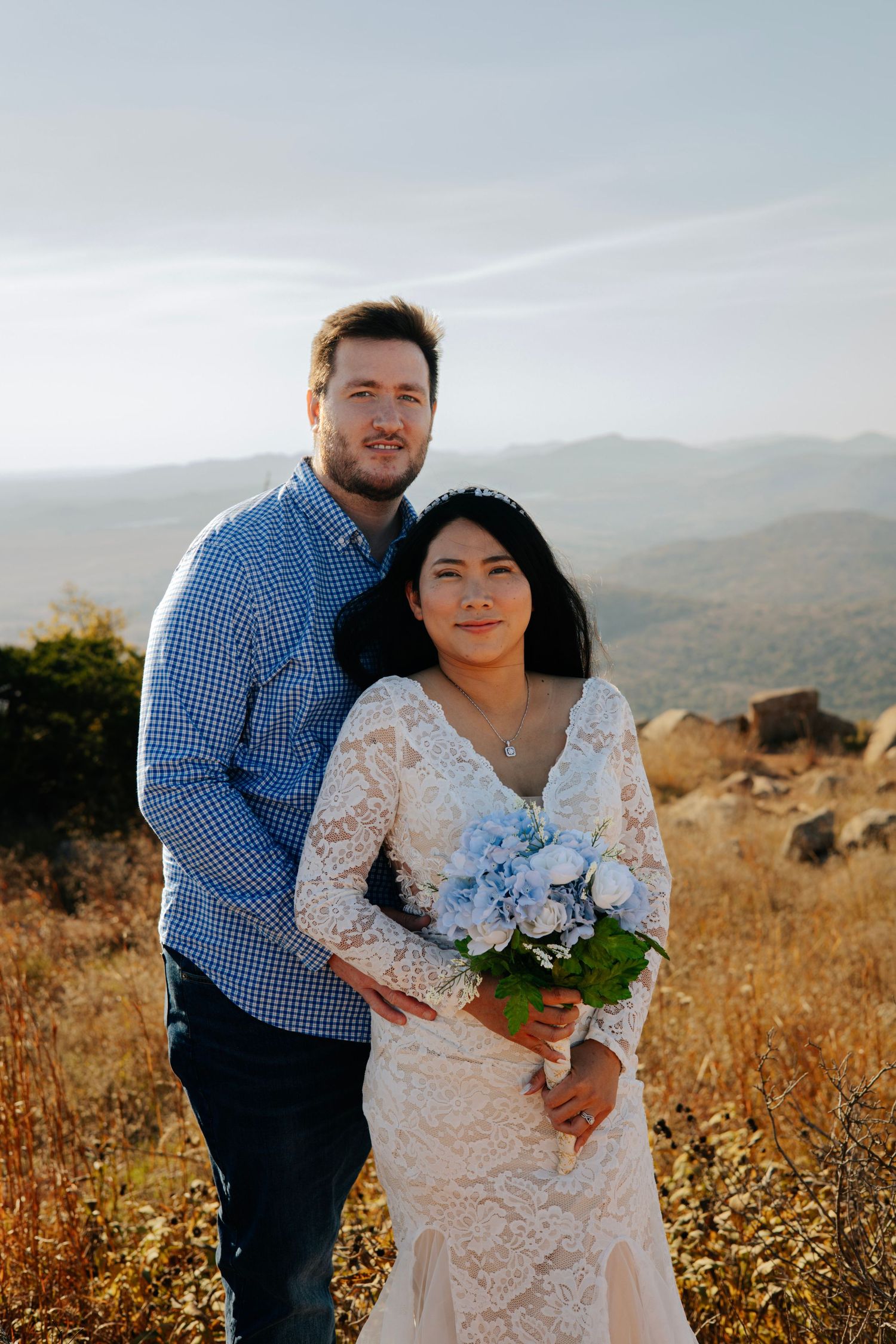 A couple poses together on a mountain overlook with scenic views behind them.