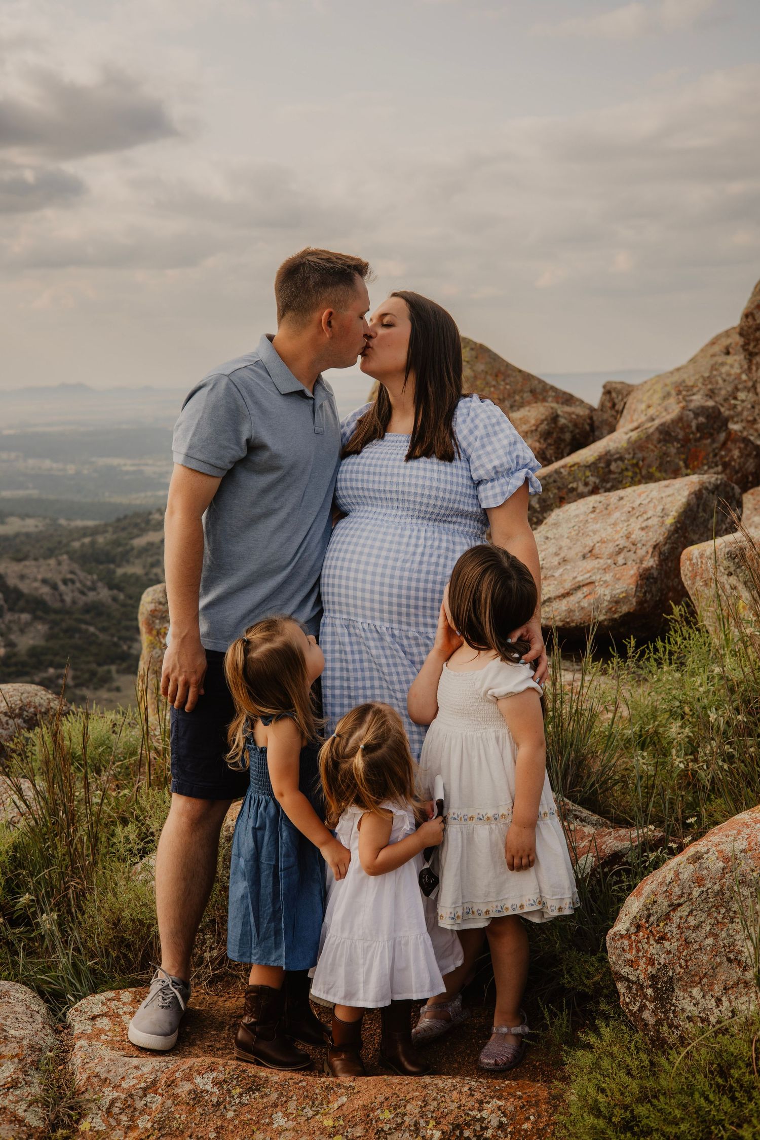 Family maternity photoshoot on rocky mountain overlook during sunset.