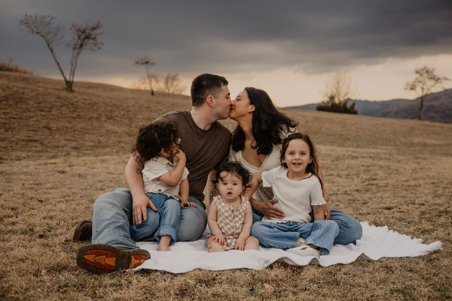 Family sitting together on blanket during sunset in rustic field setting.