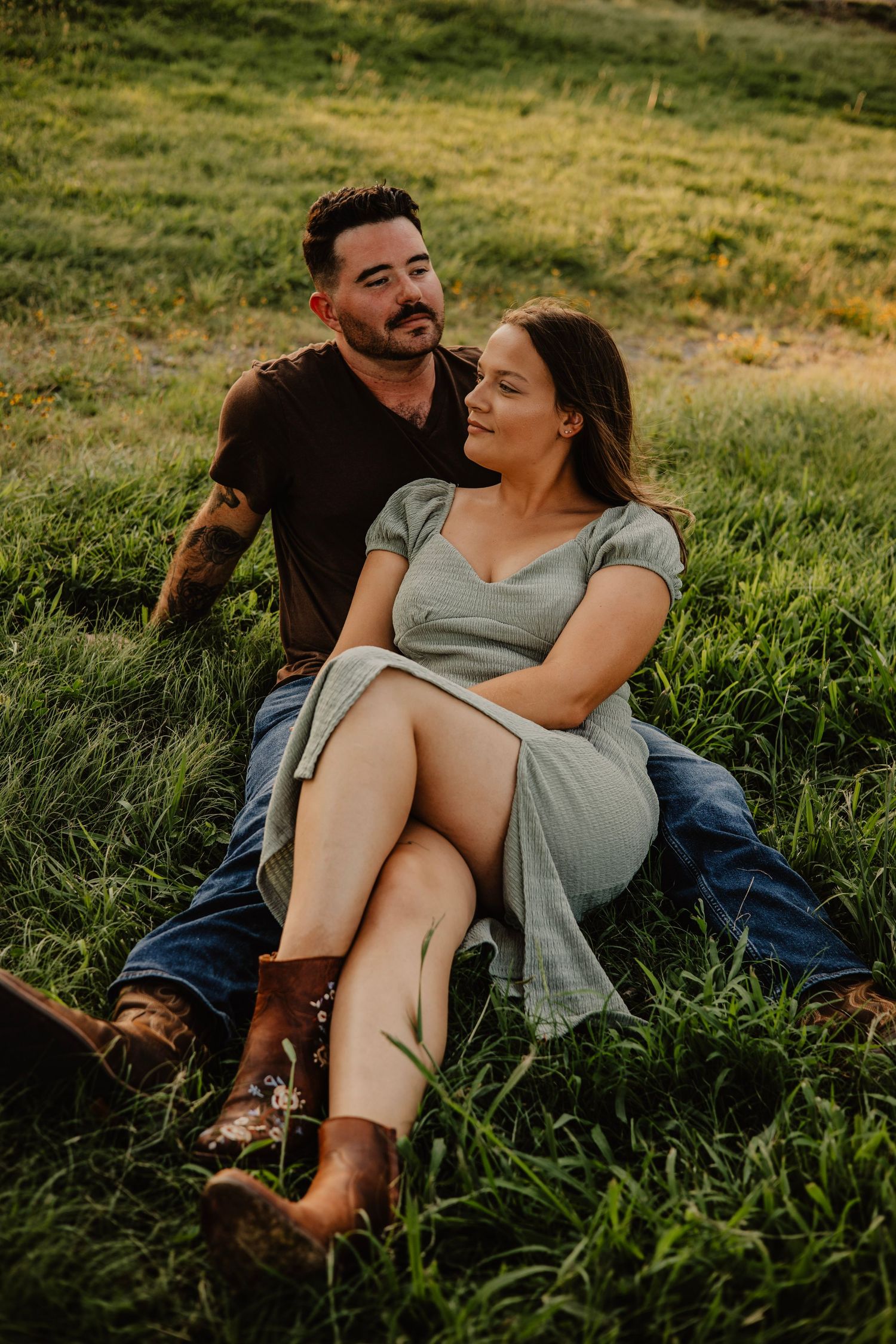 Couple relaxing together on grassy hillside during golden hour photoshoot.