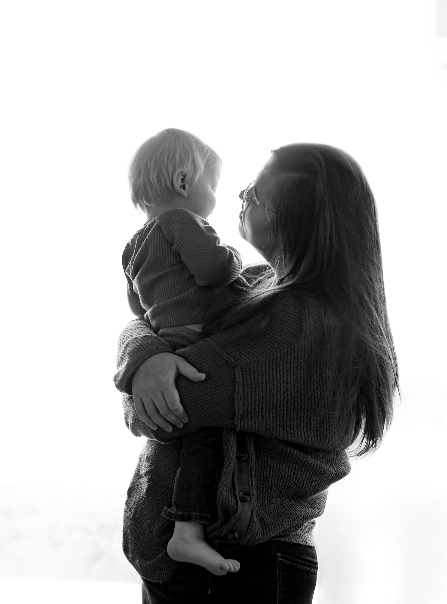 Black and white portrait of tender embrace between parent and child against white background.