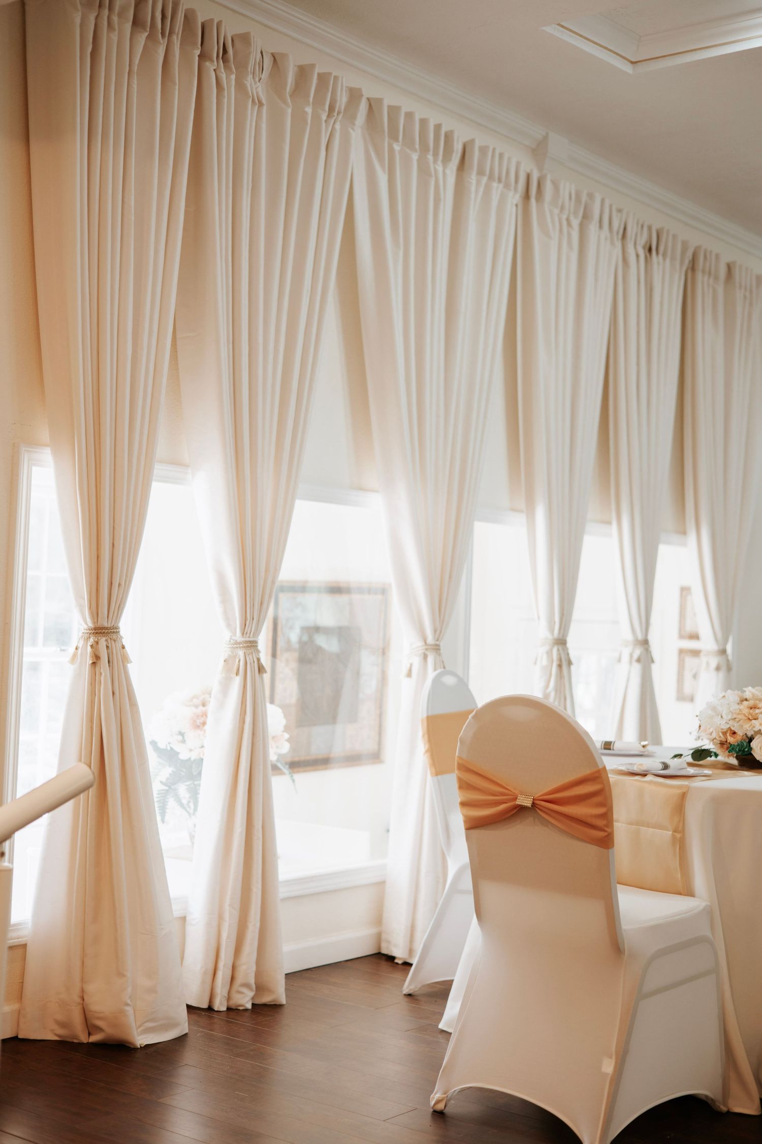 Floor-to-ceiling white curtains with peach accents line the walls of an elegant wedding venue.