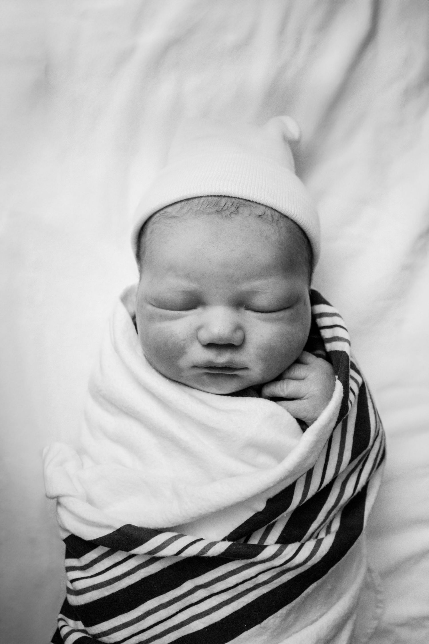 A sleeping newborn swaddled in striped blanket wearing white hat.
