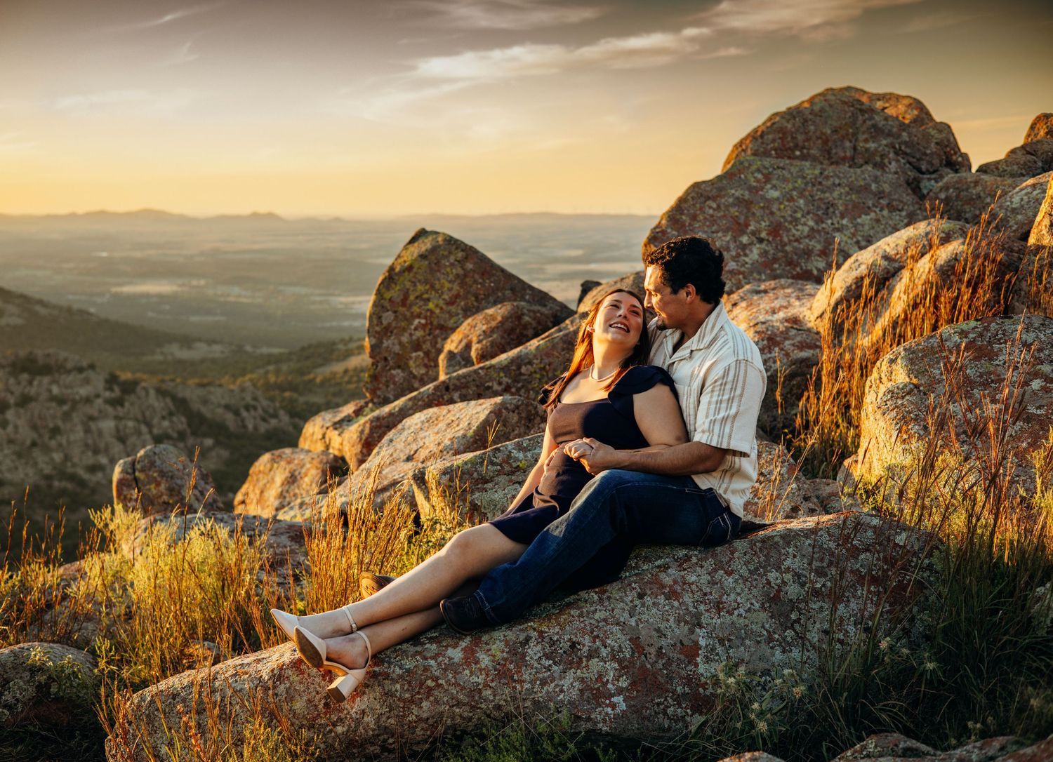 A couple sitting on rocky mountain terrain during a golden sunset.