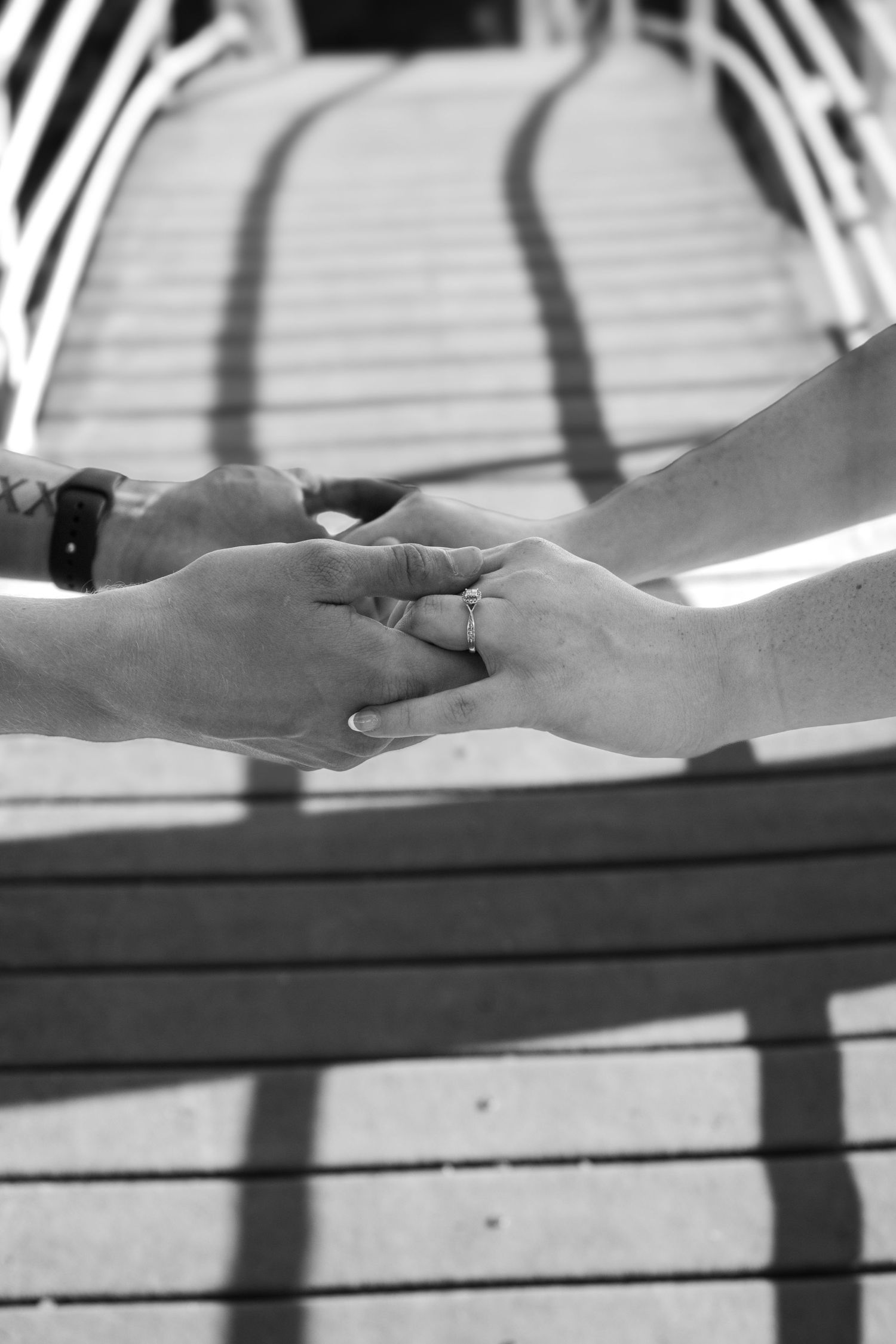 Close-up black and white photo of hands holding each other with shadows on a wooden surface.