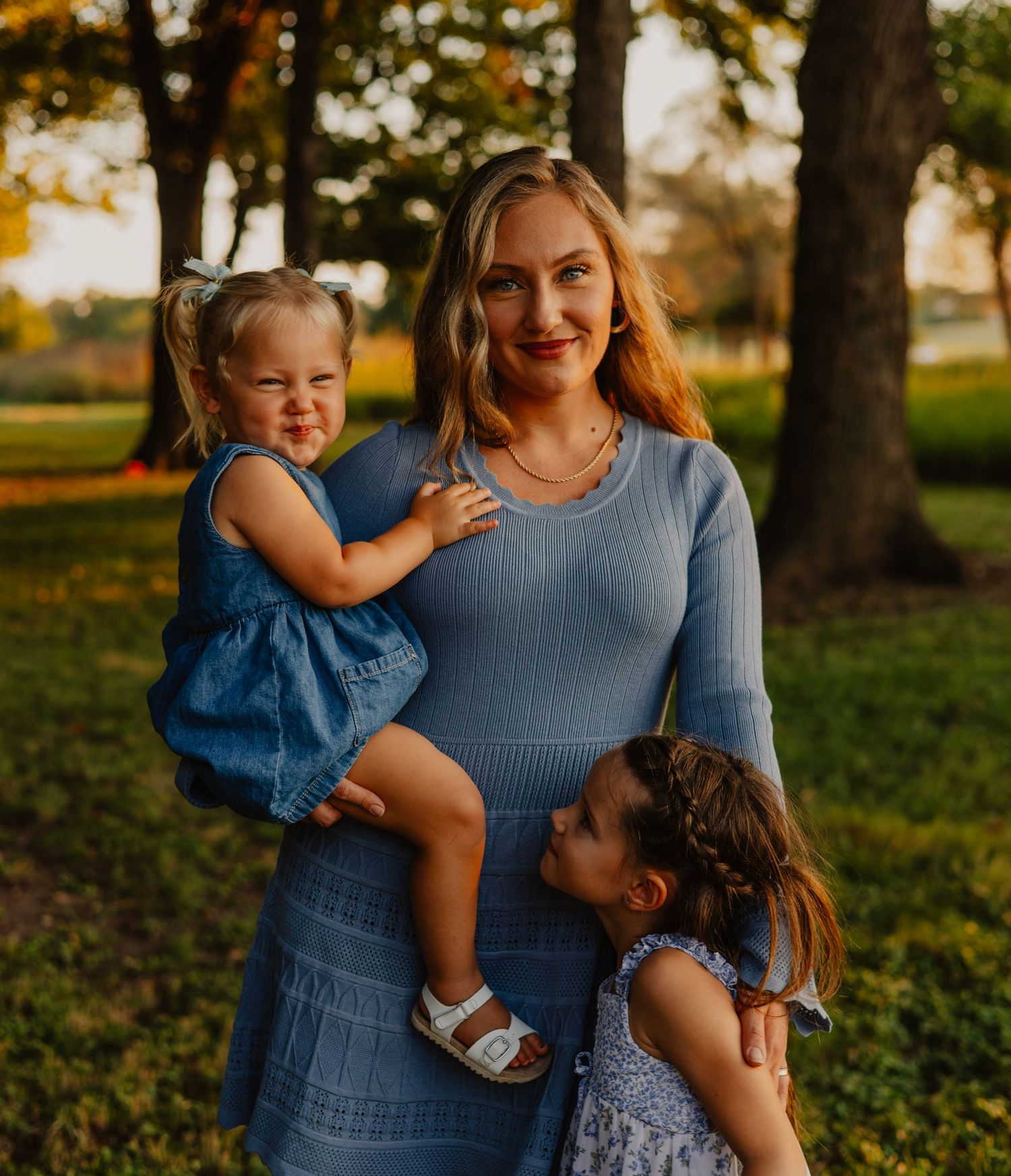 Mother and two children pose together outdoors during golden hour sunset.