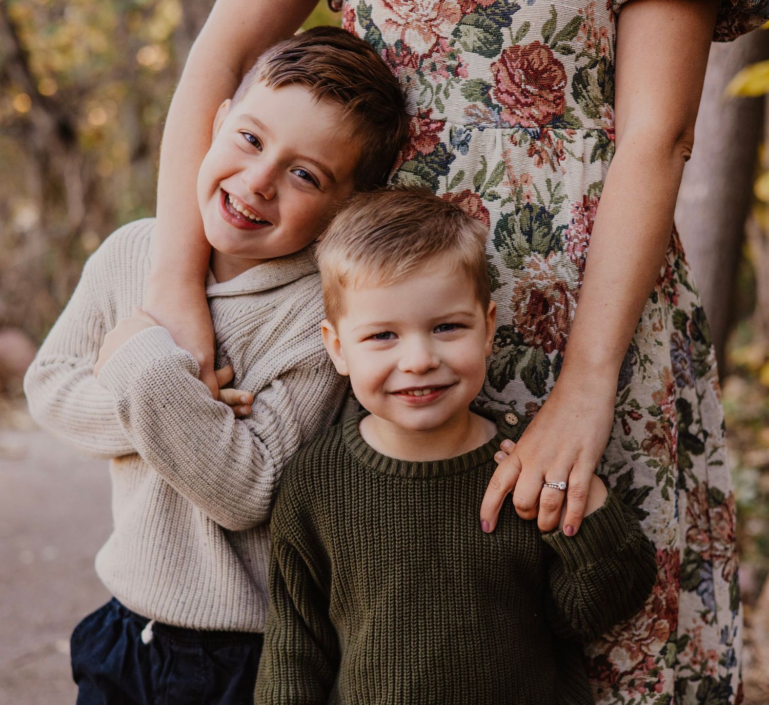 Children smile and embrace while wearing cozy sweaters in autumn setting.