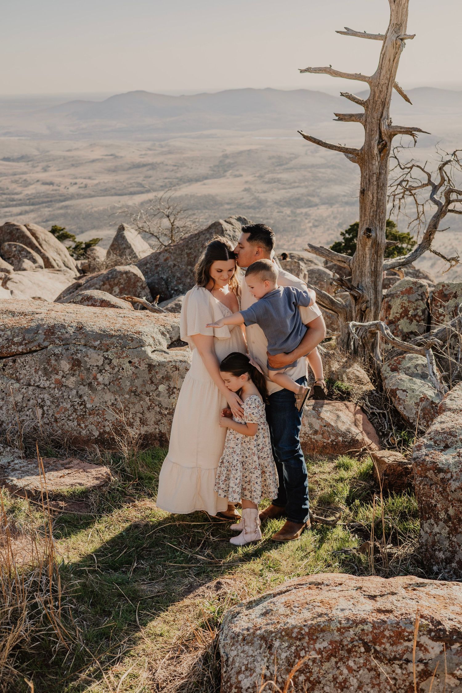 A couple shares an intimate moment together on a rocky mountain overlook with a scenic valley vista in the background.