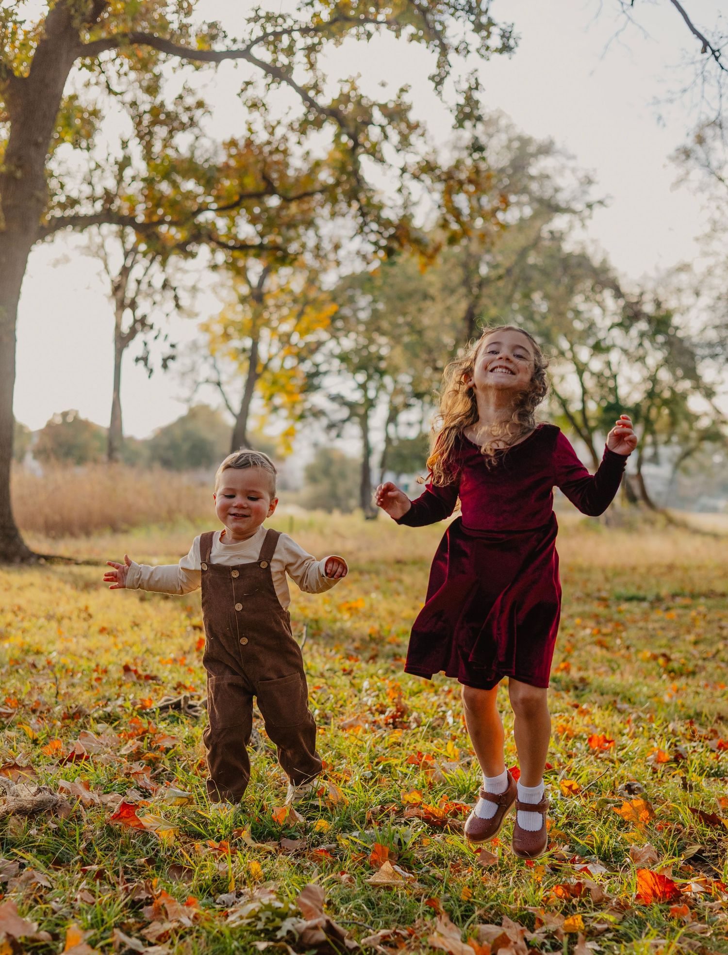 Two children jumping with joy among fallen autumn leaves in golden sunlight.