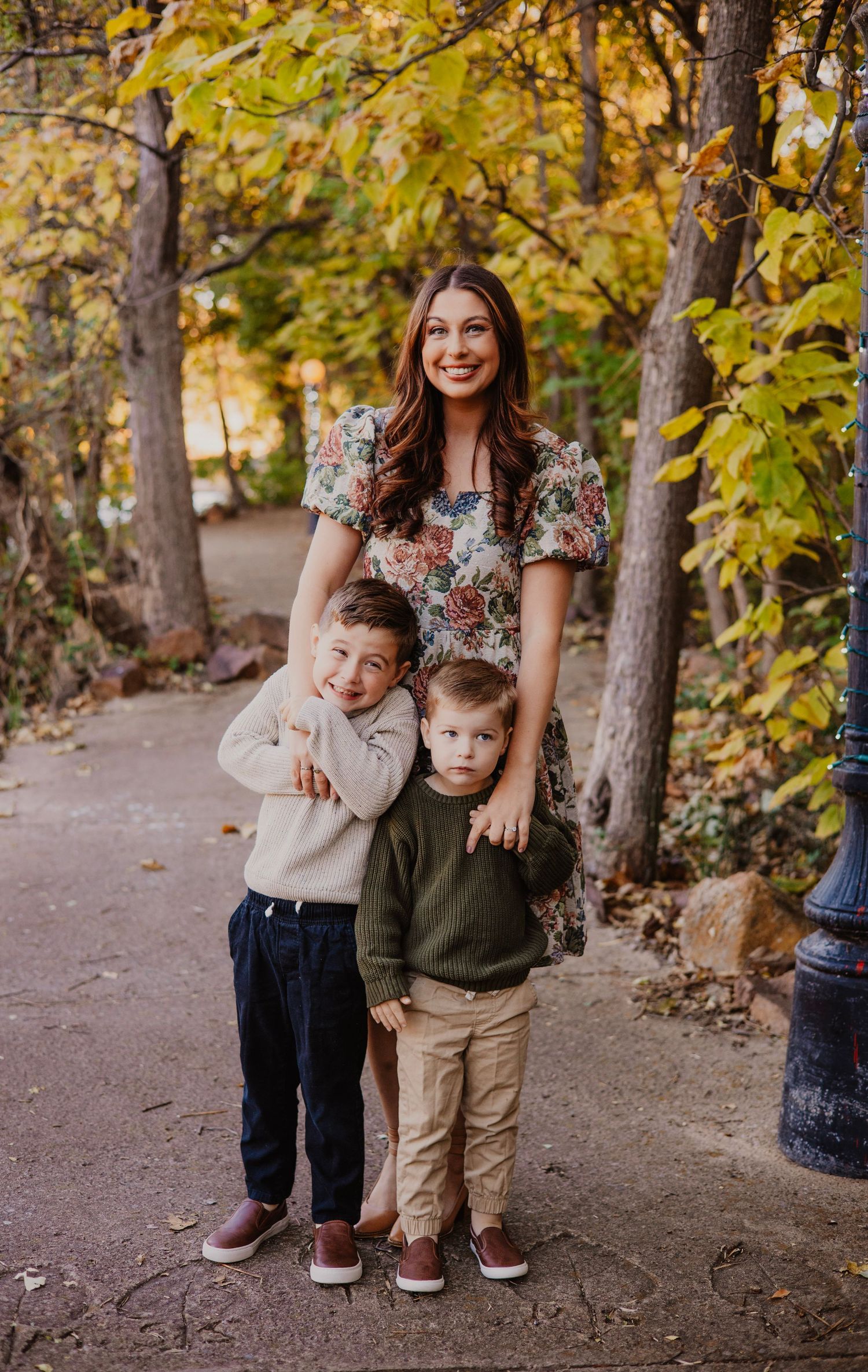 Family poses on autumn path surrounded by yellow-leaved trees.