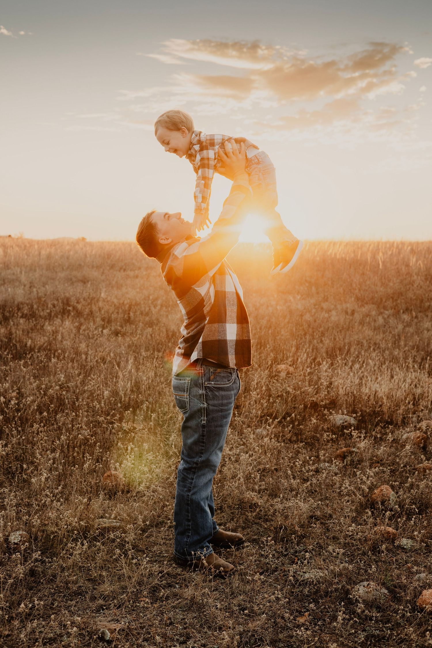 Silhouette of parent lifting child against dramatic sunset in field.